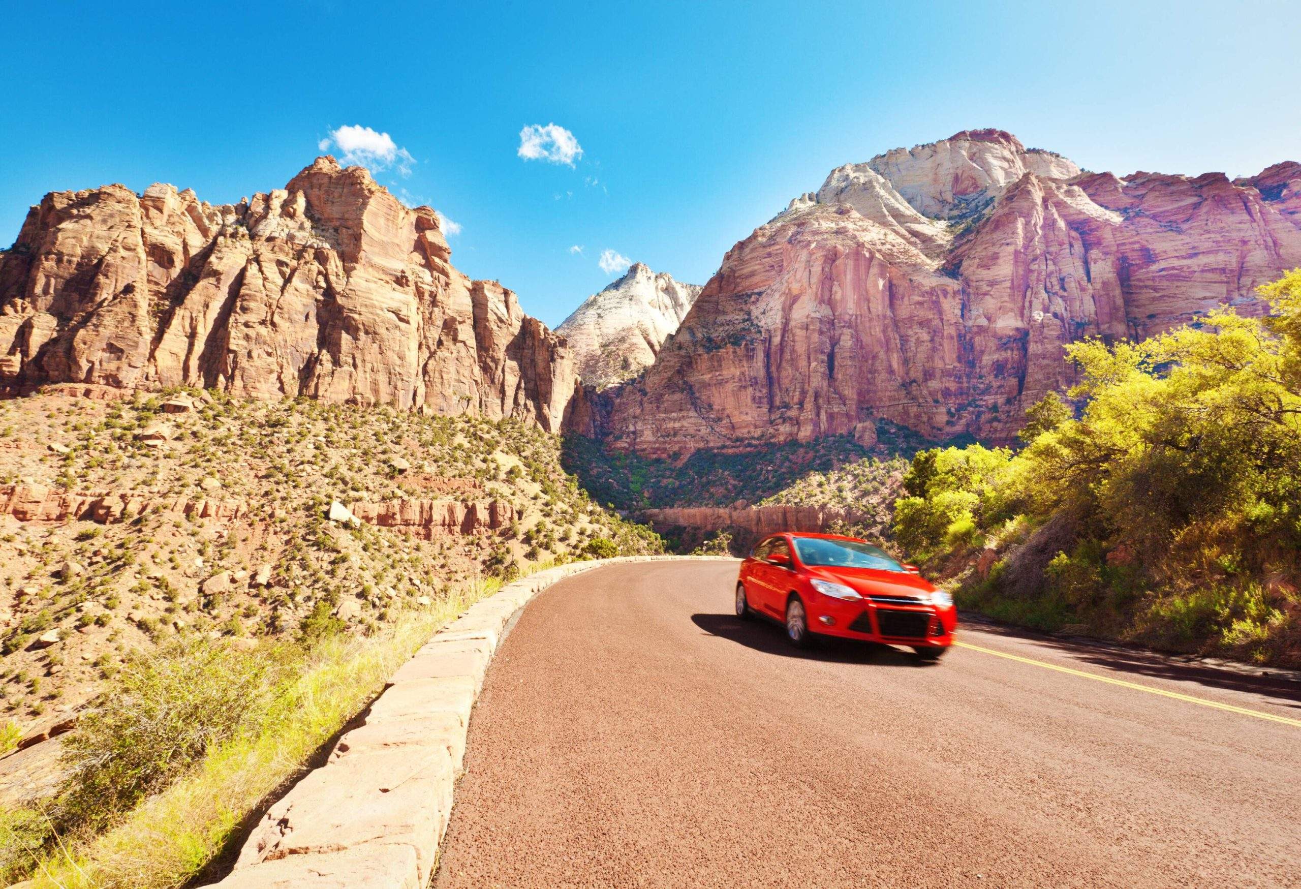 A vibrant red car cruises along the winding mountain highways, embracing the scenic beauty of the majestic peaks and panoramic vistas that surround it.