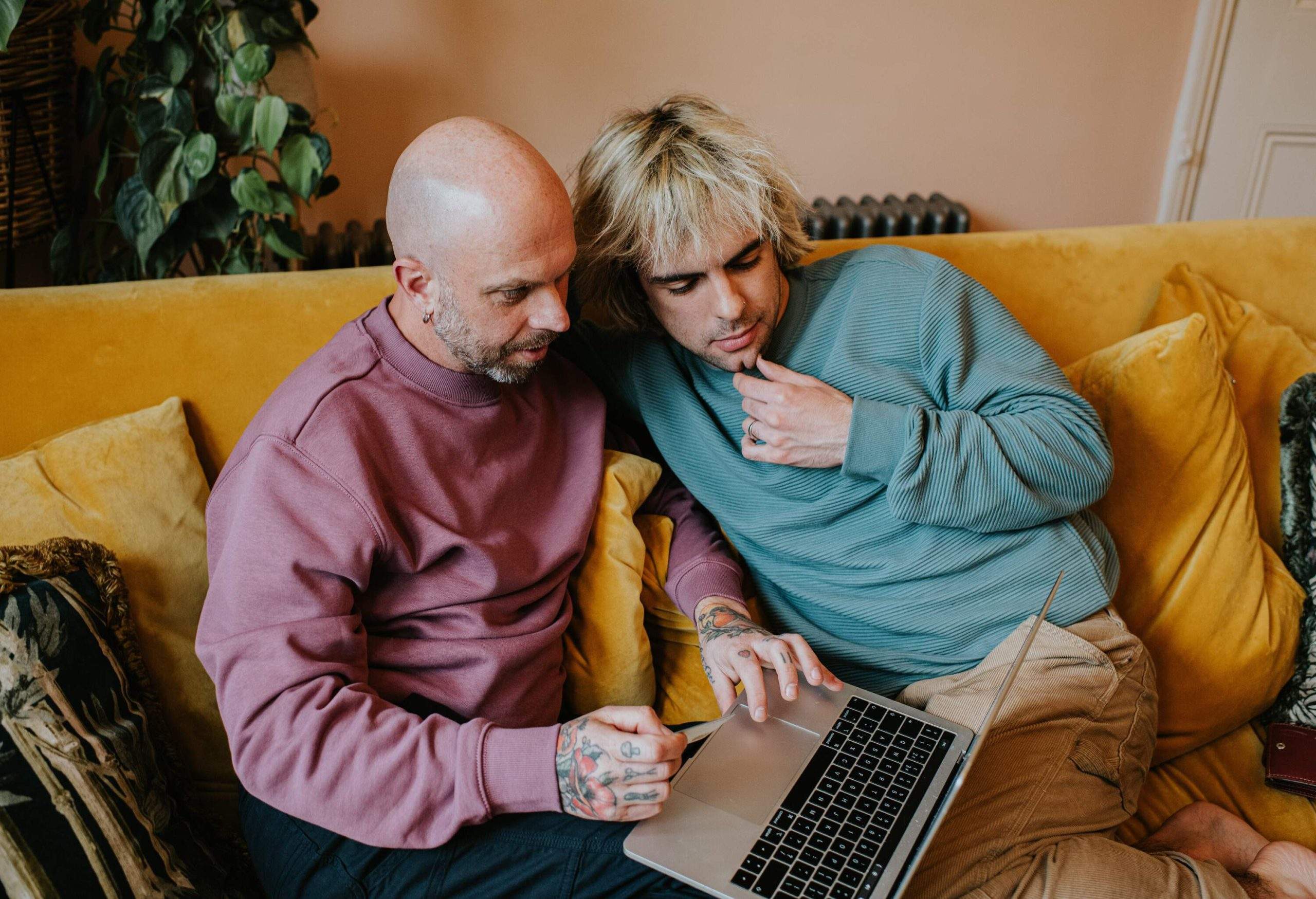 A male couple shares a laptop while sitting on the yellow couch.