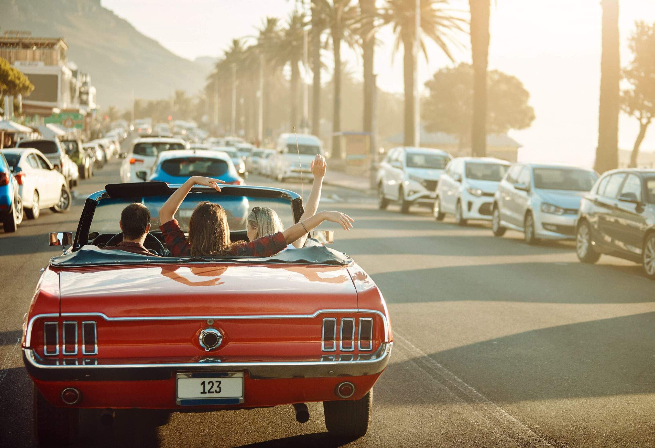 A joyful group of young friends captures the essence of a summer road trip, cruising in a vibrant red convertible car amidst the bustling traffic.