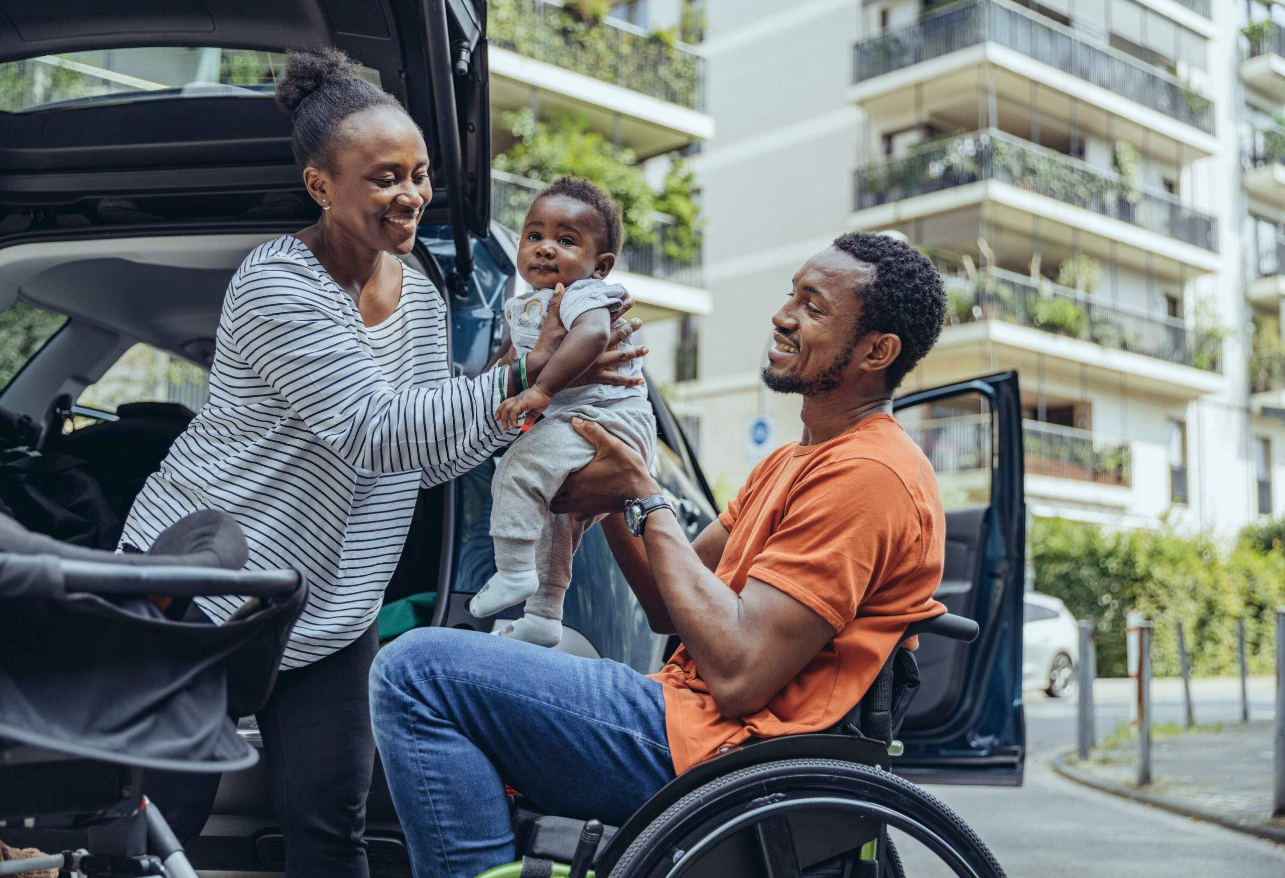 A man in a wheelchair handing a baby over to a woman.