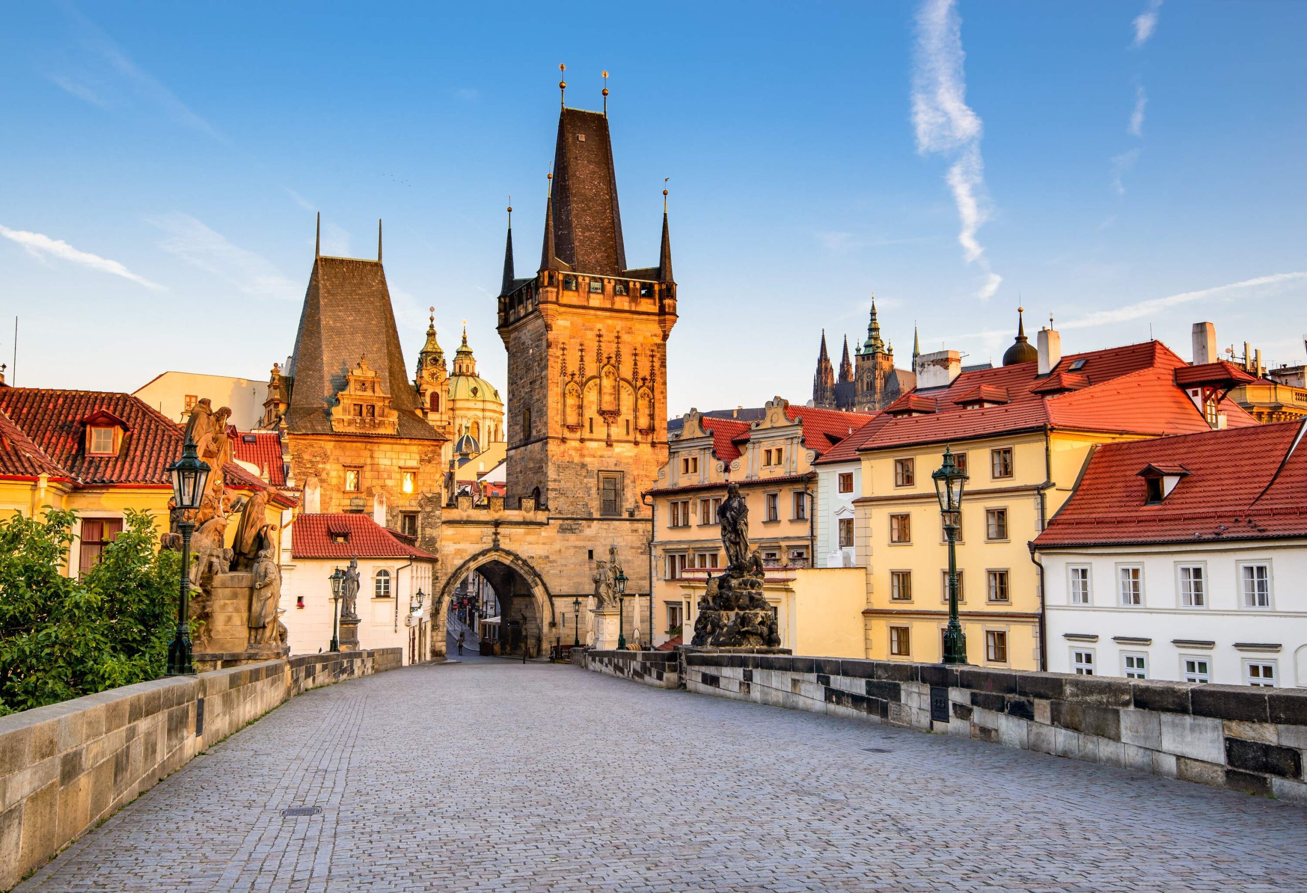 A paved walkway on a bridge across a cluster of adjacent city buildings towards an arch entrance of a gateway tower.