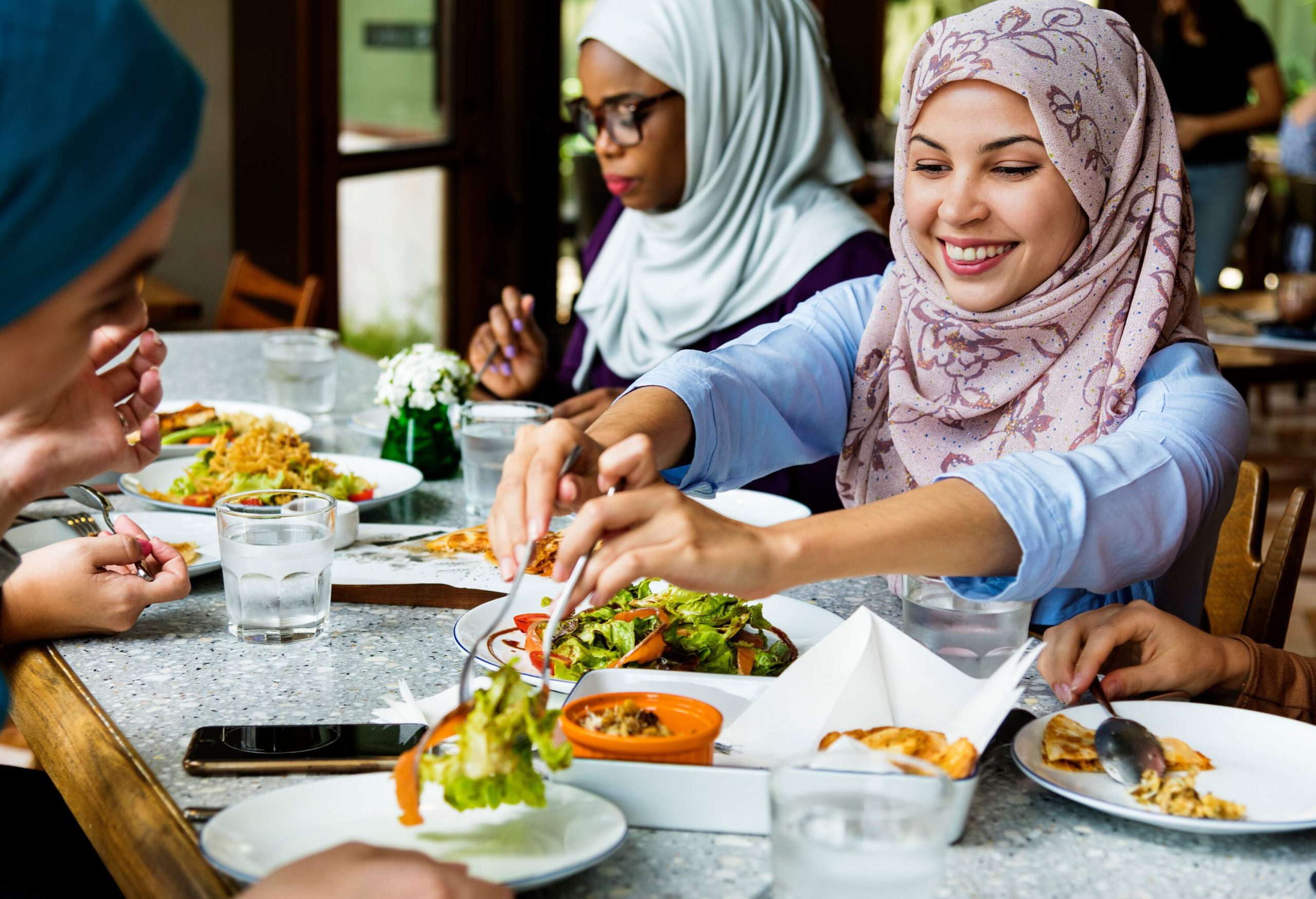 Happy women in hijab shares various dishes on white plates.