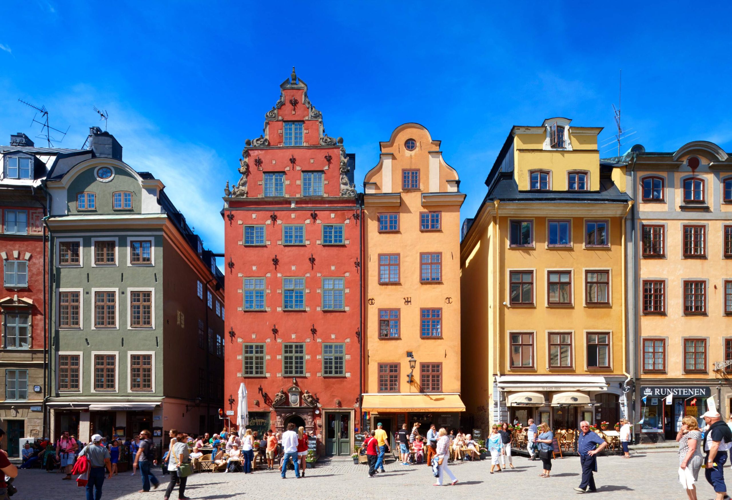 A row of colourful buildings with glass windows along a crowded public square.