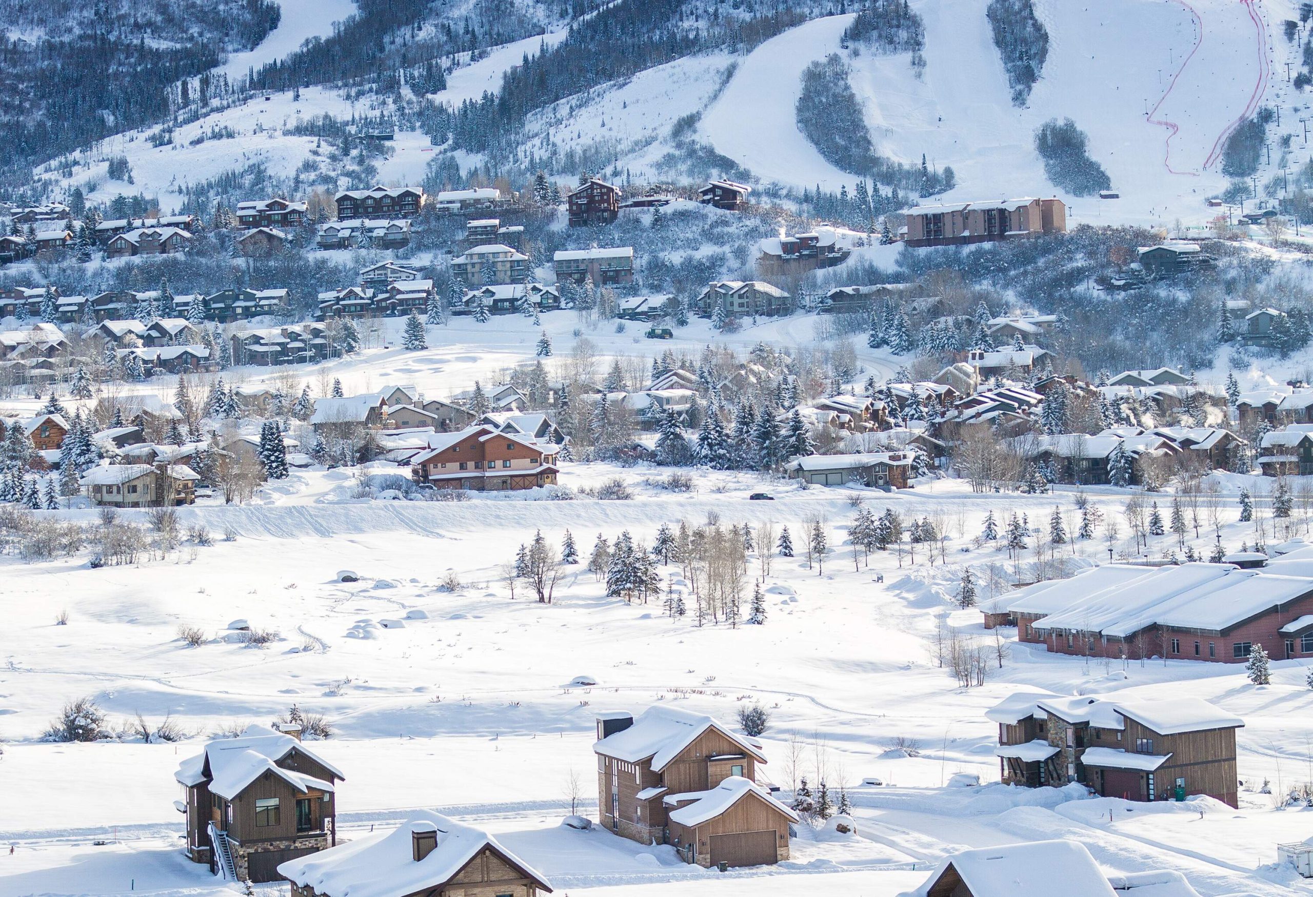 Residential and ski resort buildings in the valley of rolling snow-capped forested mountains.