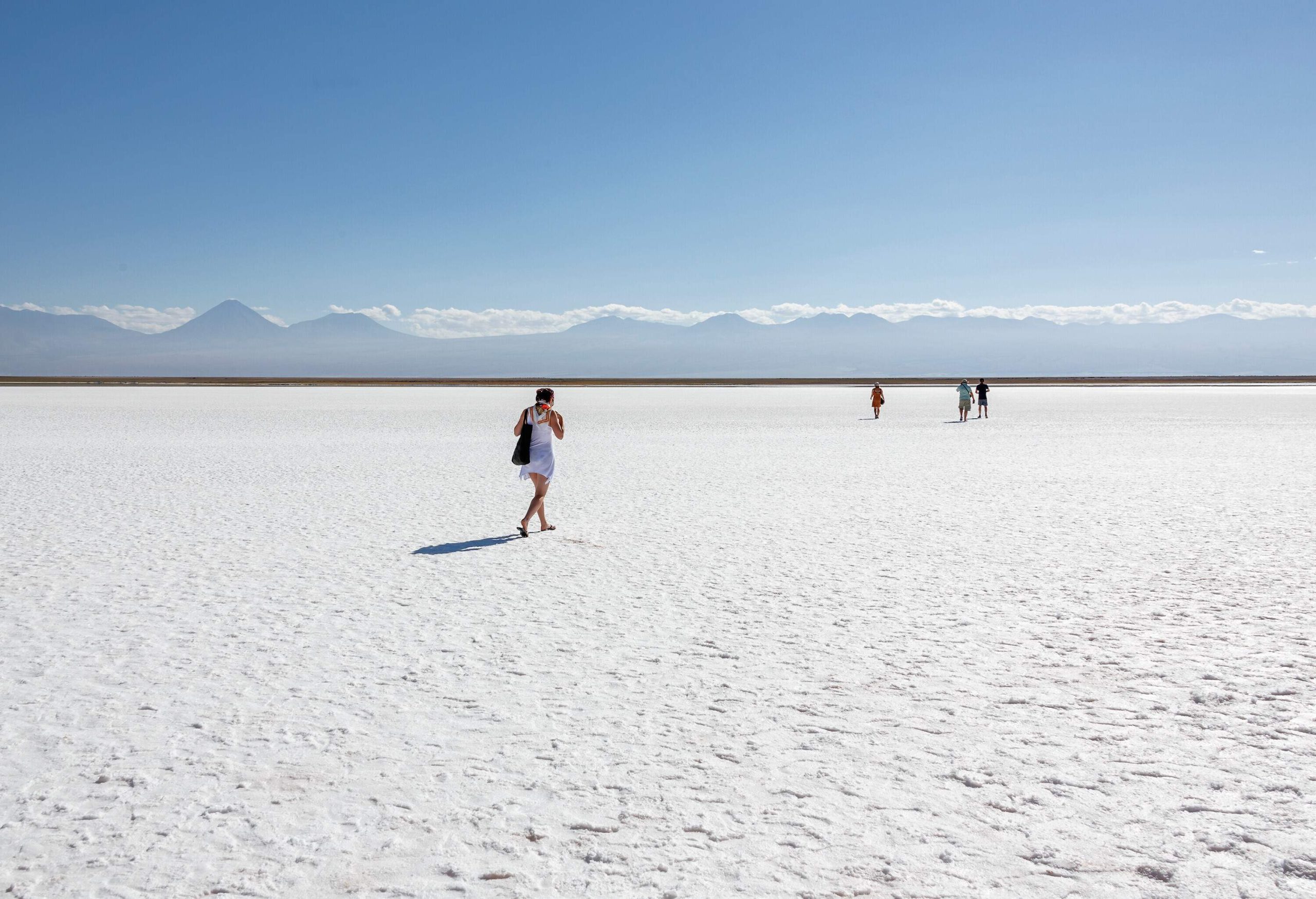 People pass through a white land towards a mountain range covered with clouds from afar under a clear blue sky.