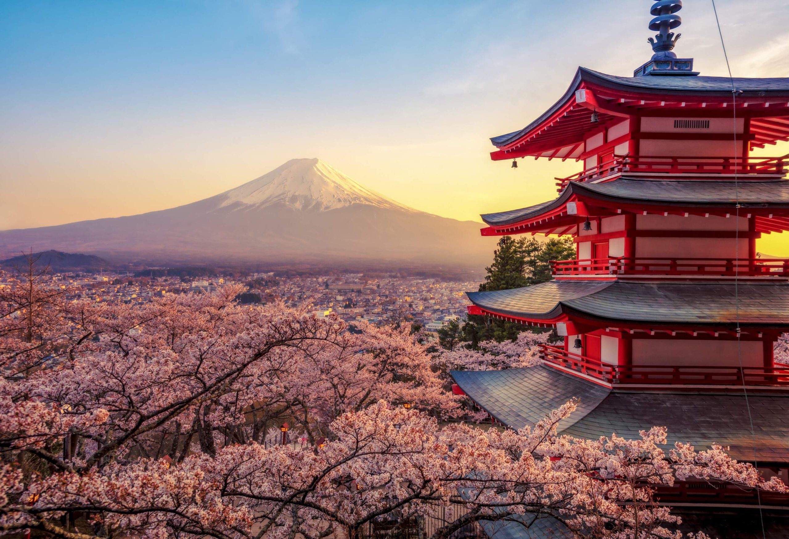 A pagoda rising over cherry blossom trees with Mt. Fuji in the background.