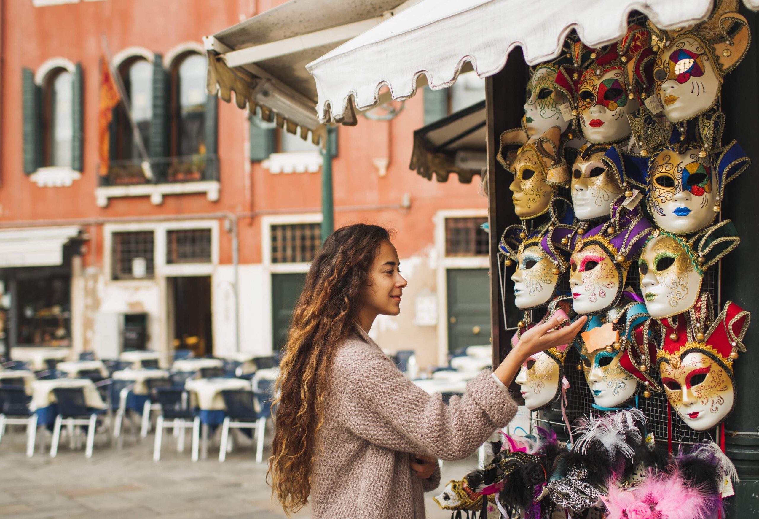 A long-curly-haired lady looks at a mask displayed outside a souvenir shop.