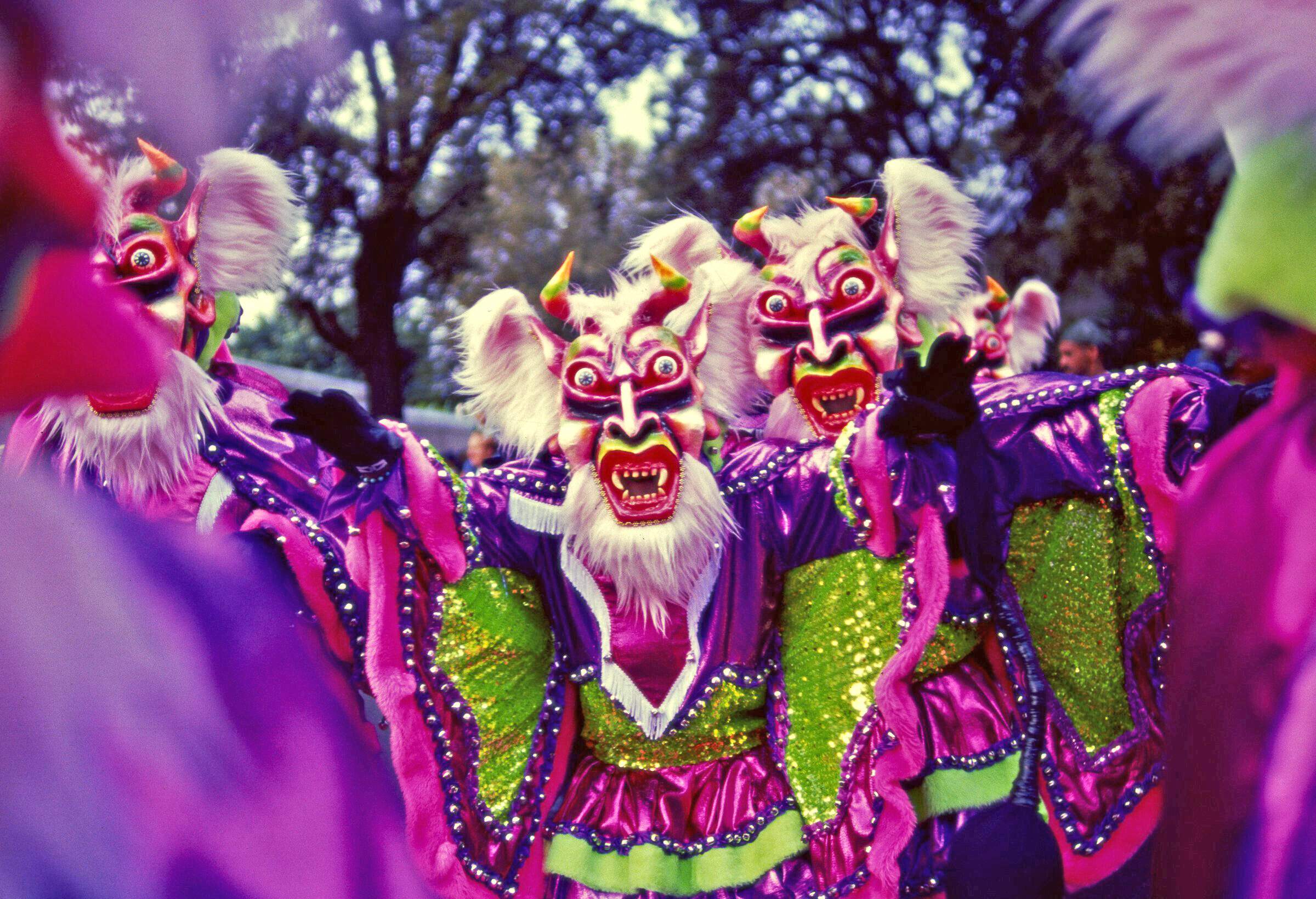 People wearing vibrant costumes and grotesque masks.