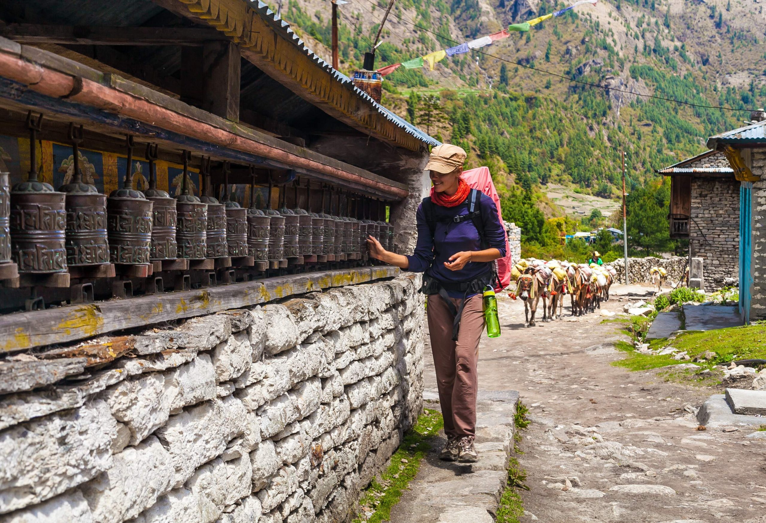 A female hiker with a camping bag touched a row of prayer wheels on a sidewalk.