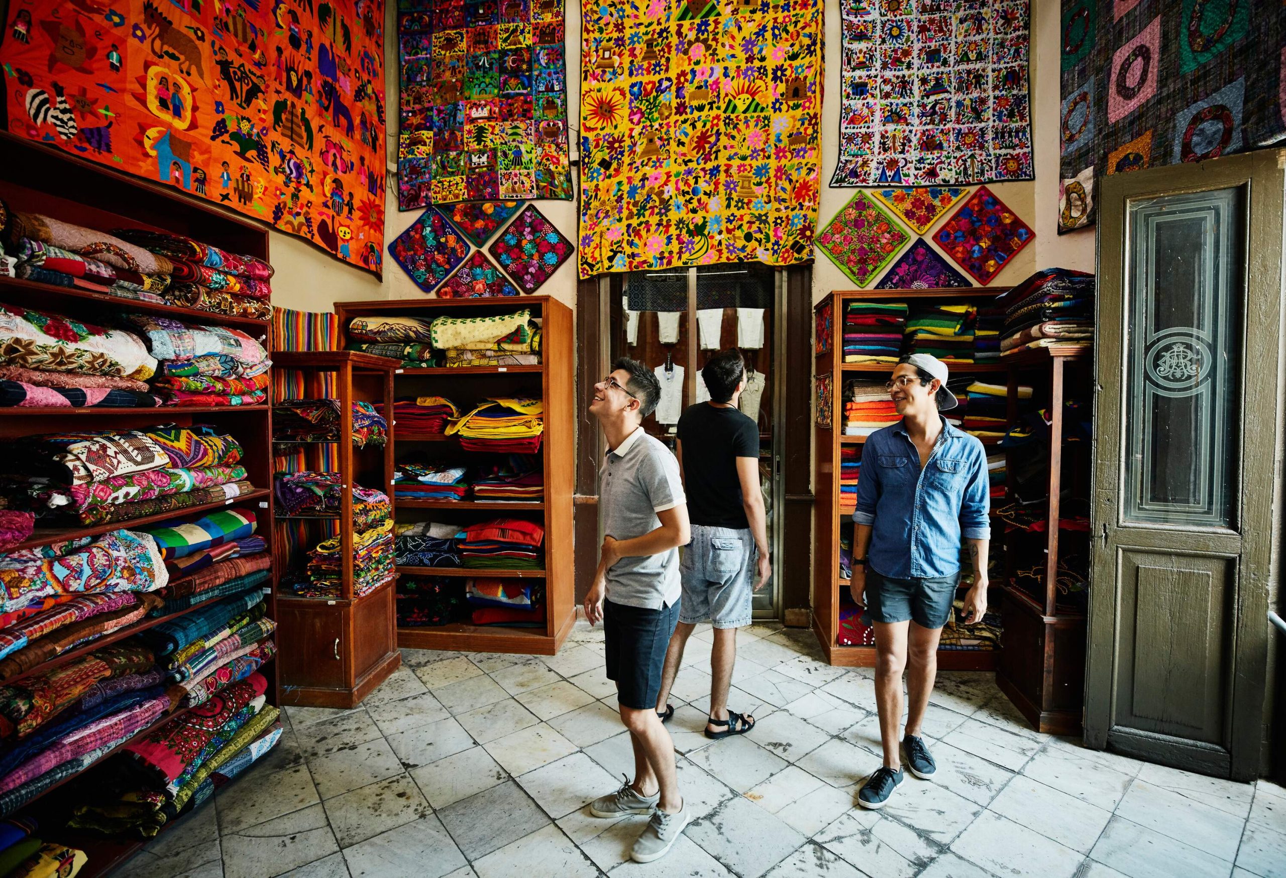Three individuals explore the enchanting world of carpets within a vibrant store, their eyes captivated by the intricately woven designs adorning the walls and shelves.
