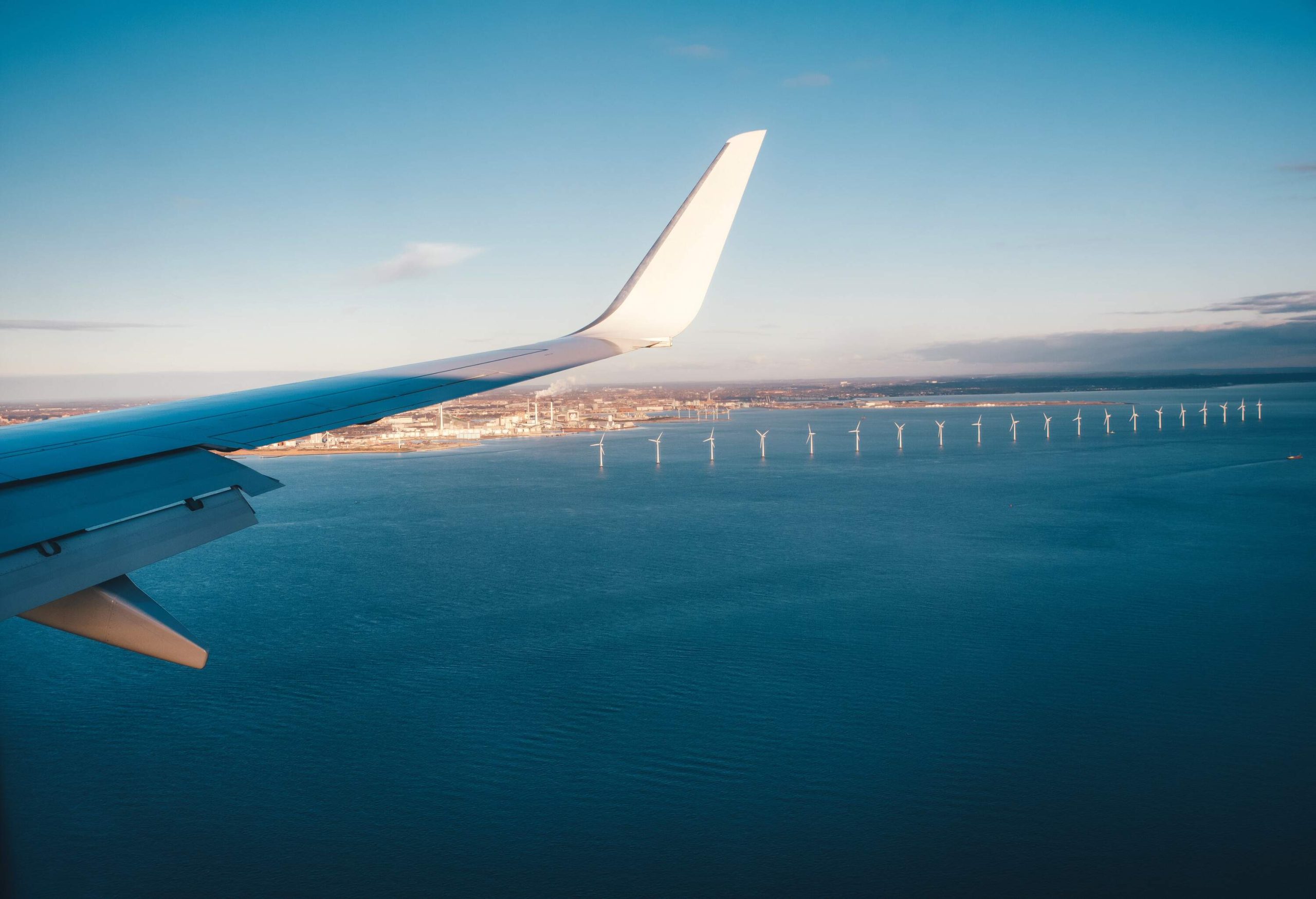 A plane's wing overlooks a sea, including a row of offshore wind turbines.