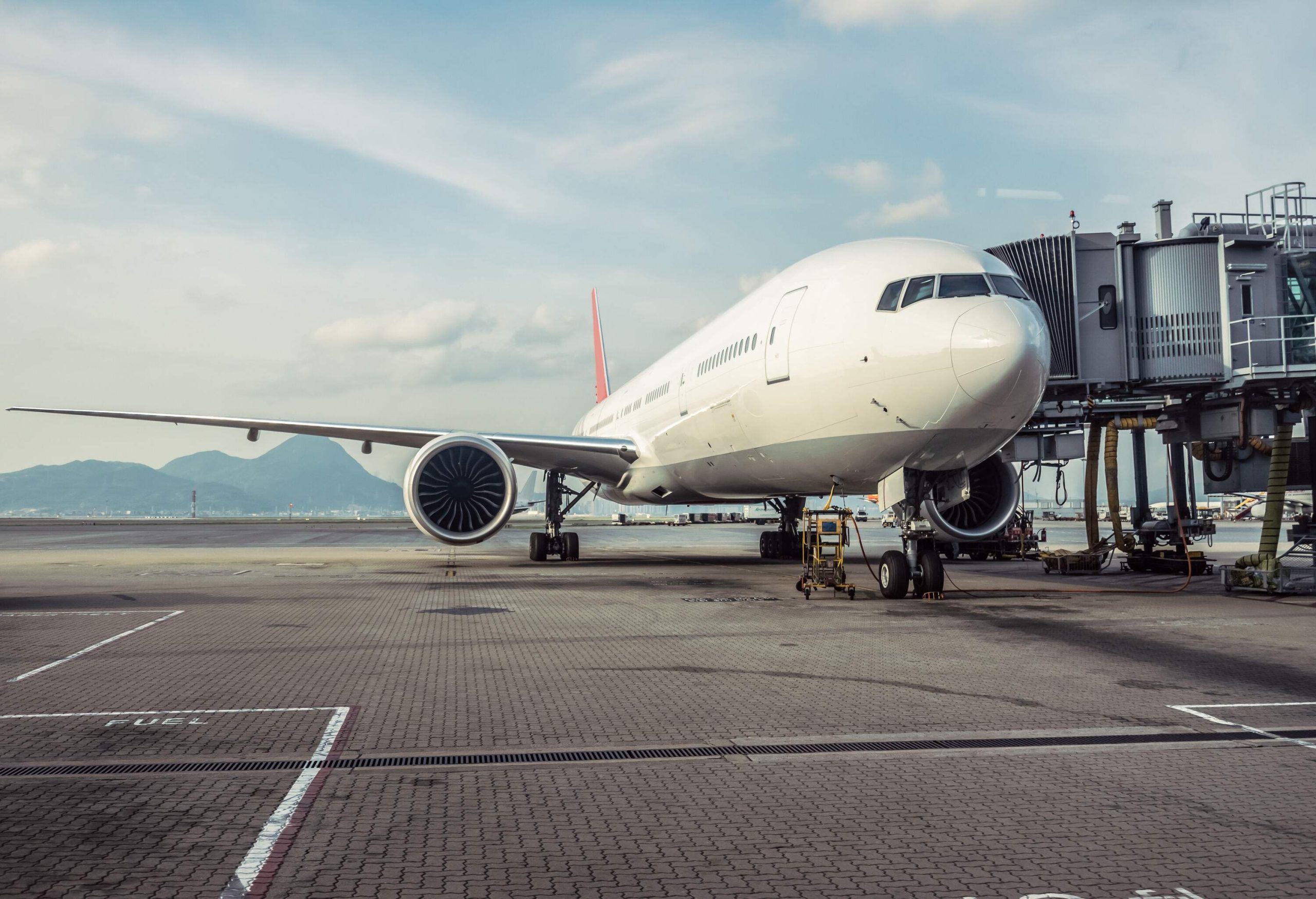 A white airplane parked at the airport terminal connected to a jet bridge.