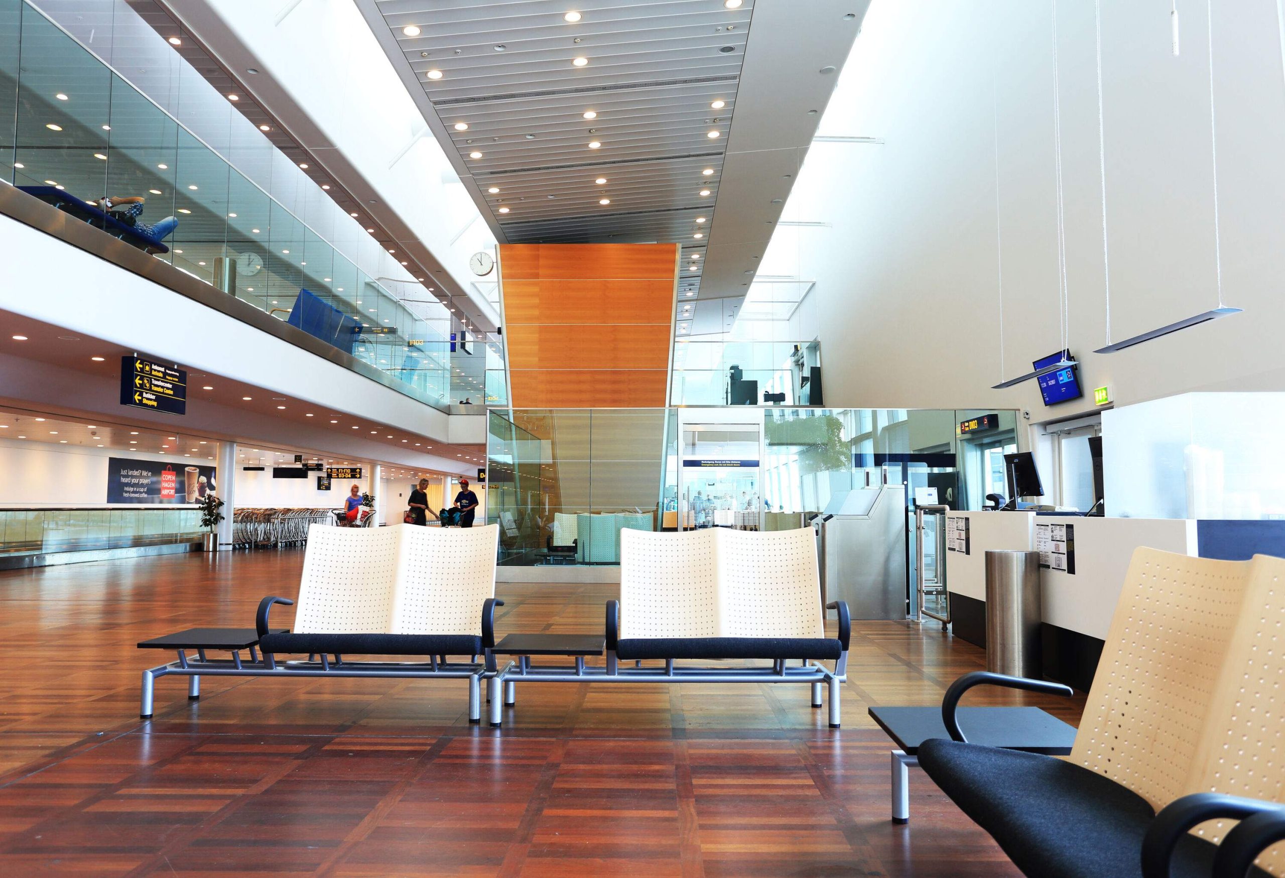 Benches with armrests and side tables on a tidy waiting hall in a brightly lighted airport.