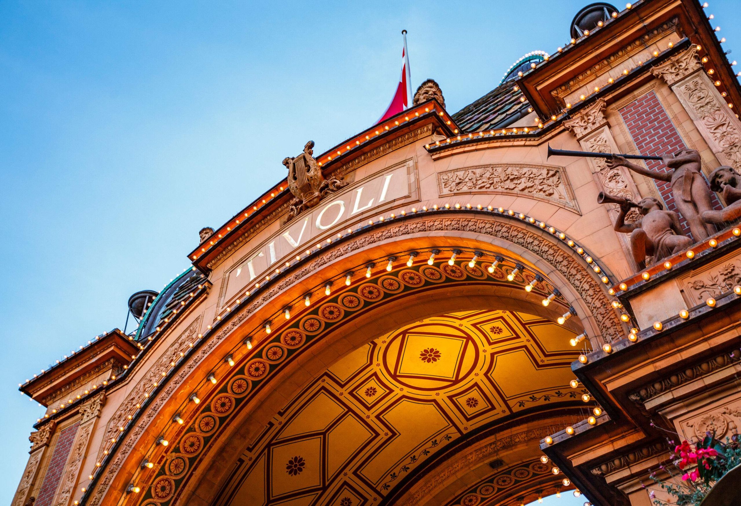 A gateway monument adorned with intricate sculptures and lighting with the words "TIVOLI" written on the arched façade.