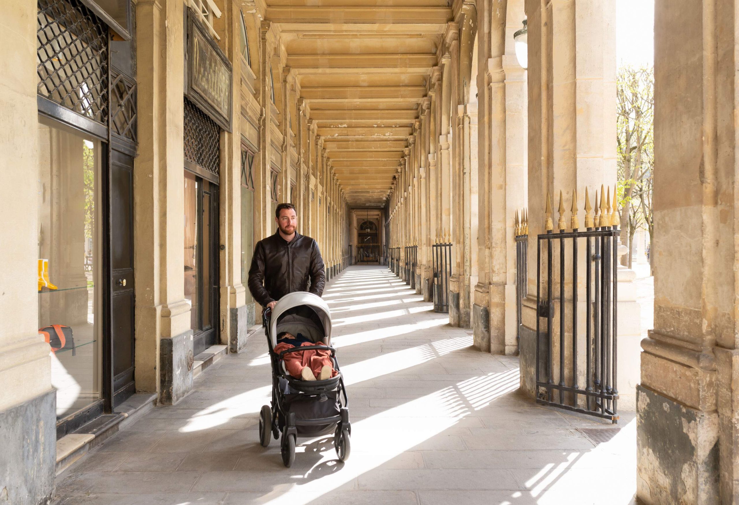 A man pushing a pram carrying a small child along the corridor of an old building.