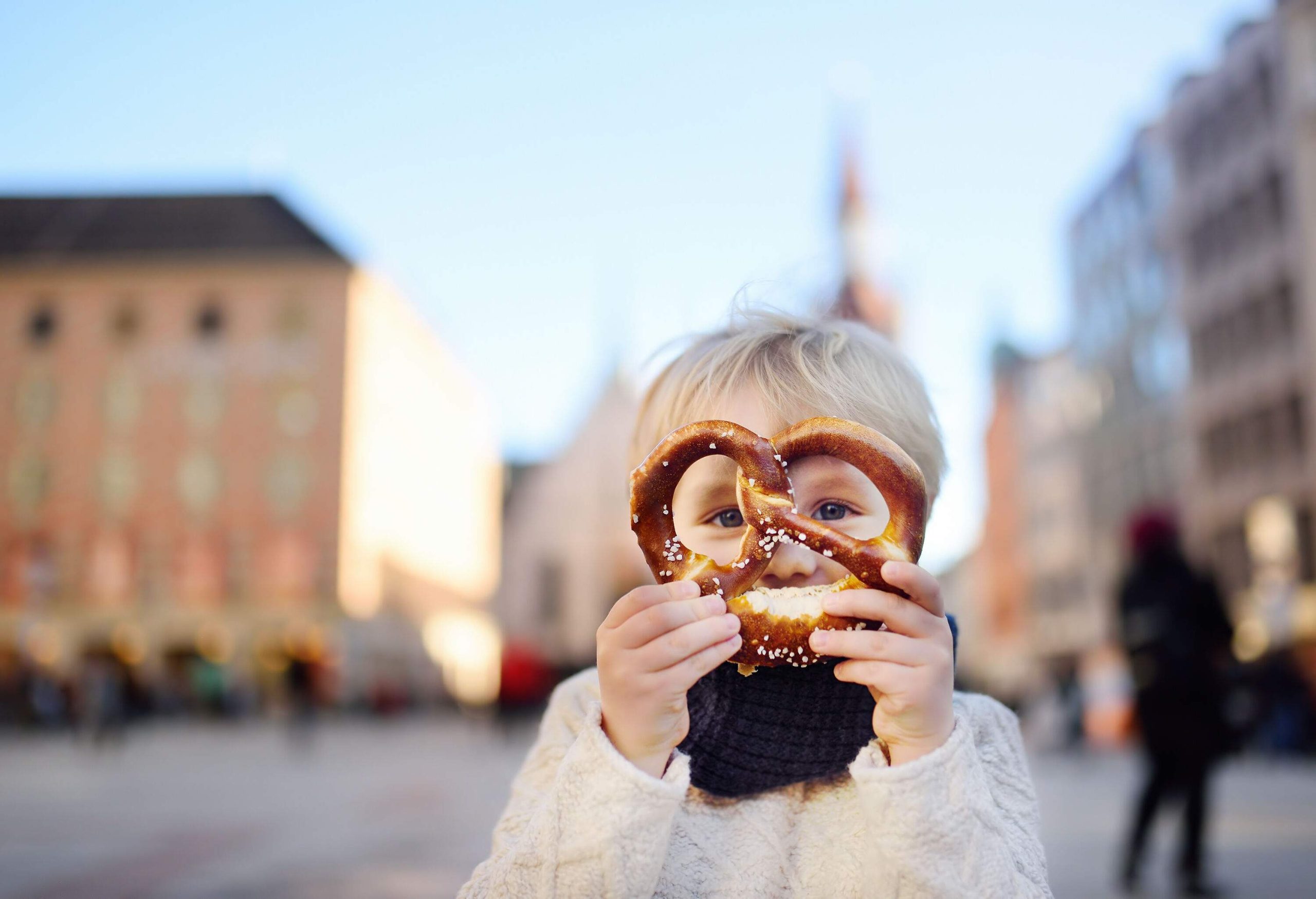 A blonde kid holding a pretzel to his face.