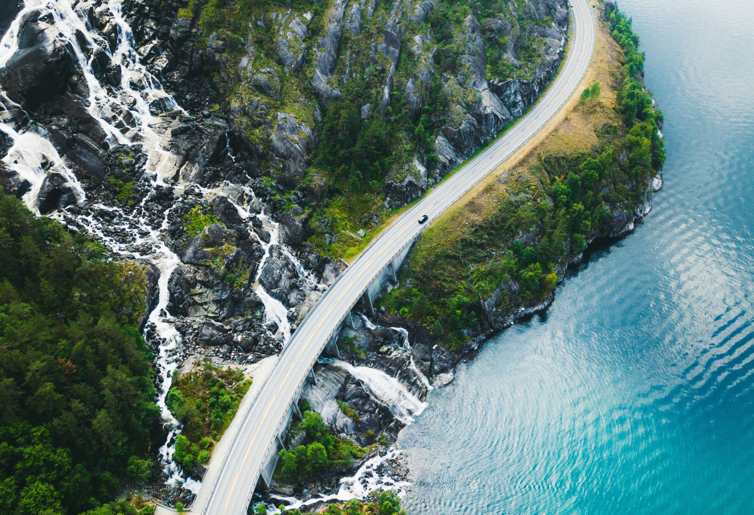A car travels on a coastal road that crosses a hillside waterfall that pours into the ocean.