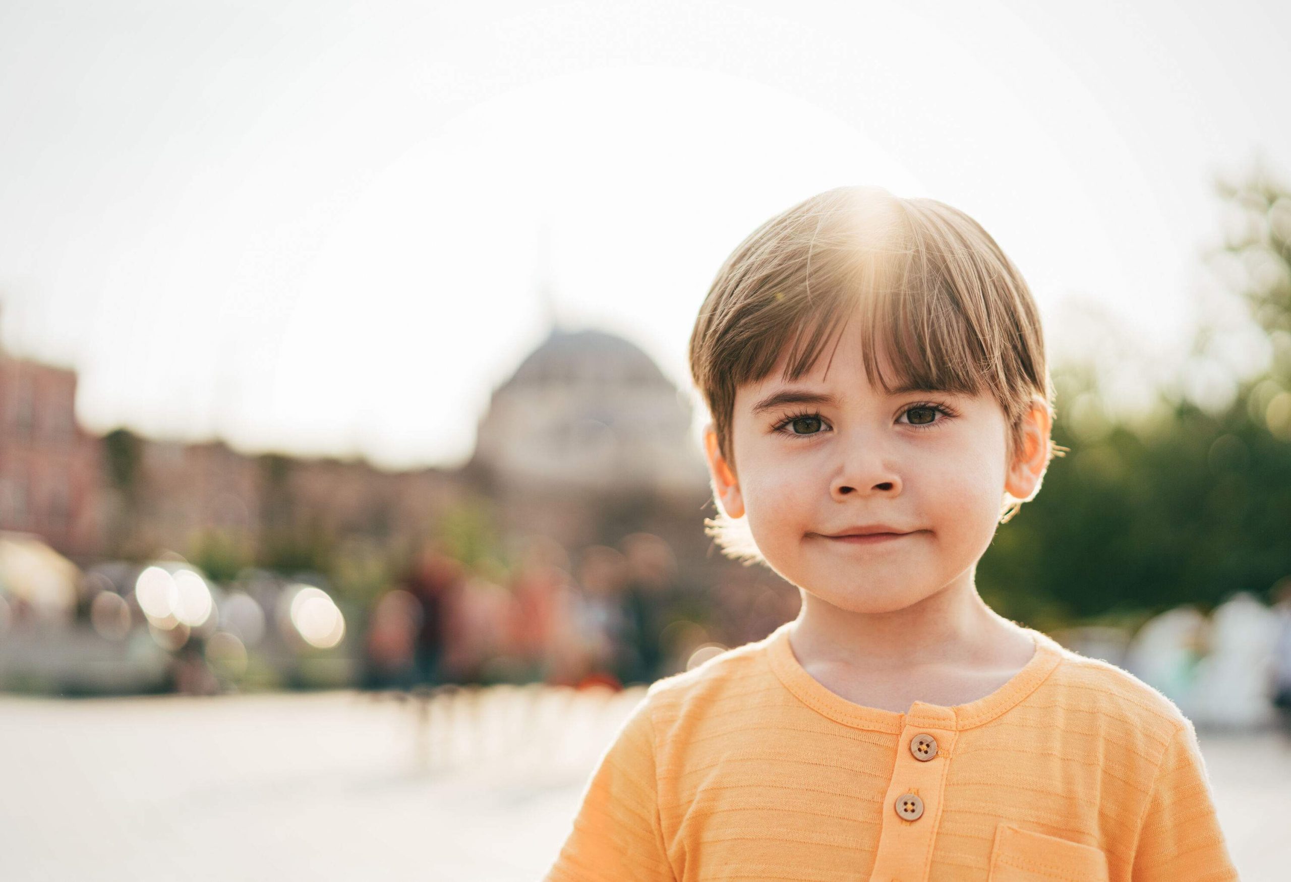 A boy in a fading gold shirt smiles against the setting sun.