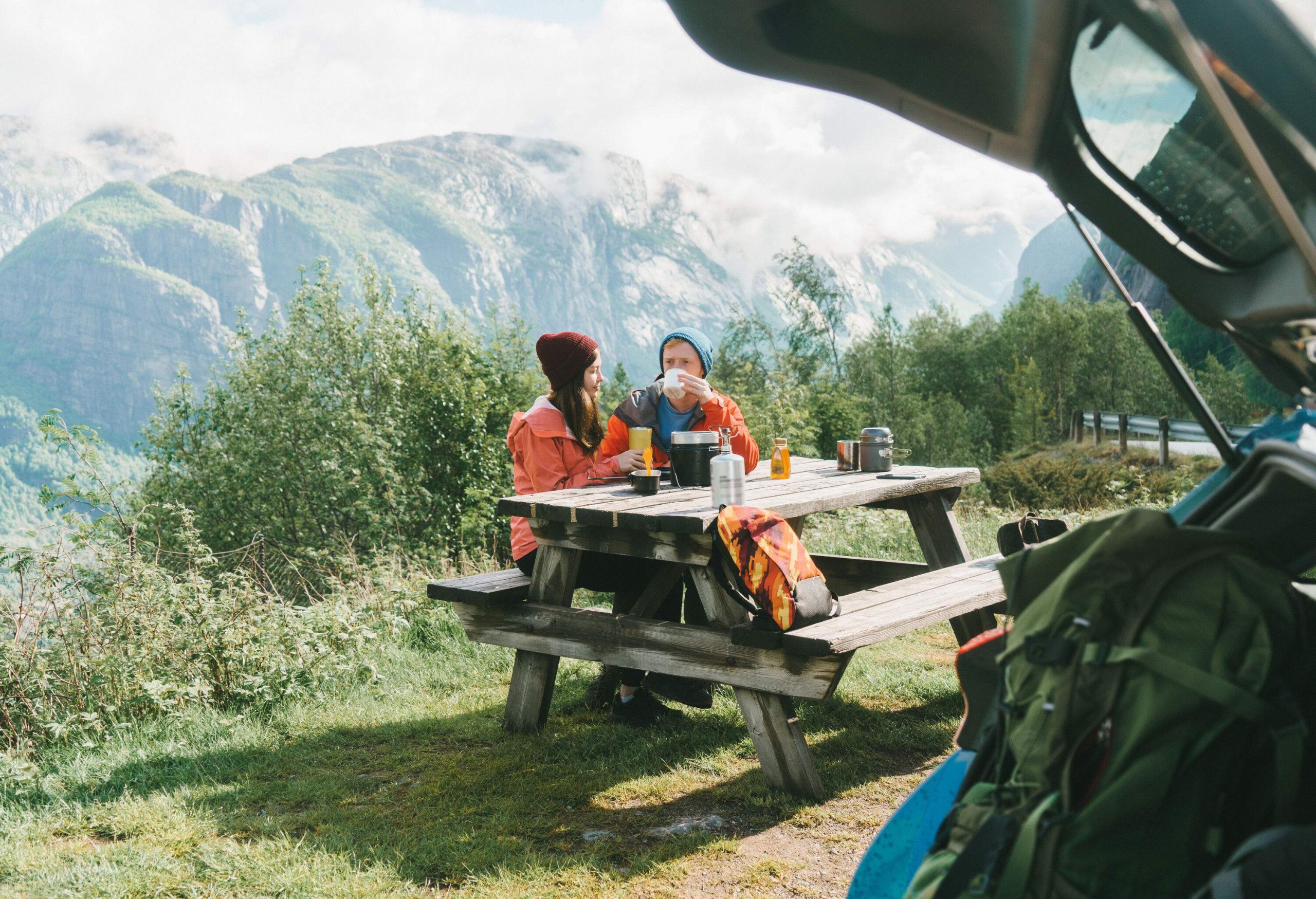 A couple in winter clothes having breakfast on a picnic table in a mountainous area.