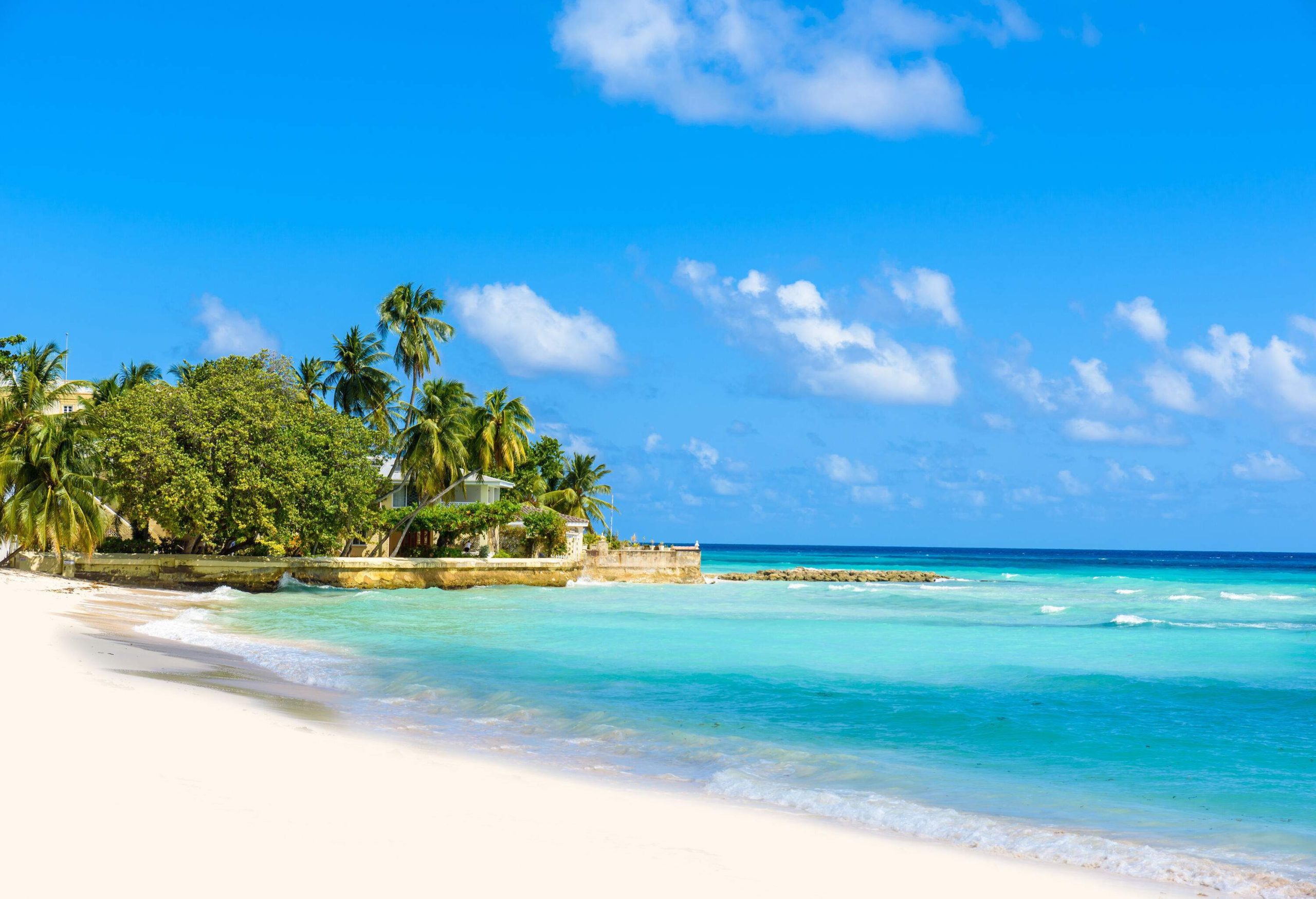 An inviting beachscape with white sand and aquamarine waters under a sunny sky.