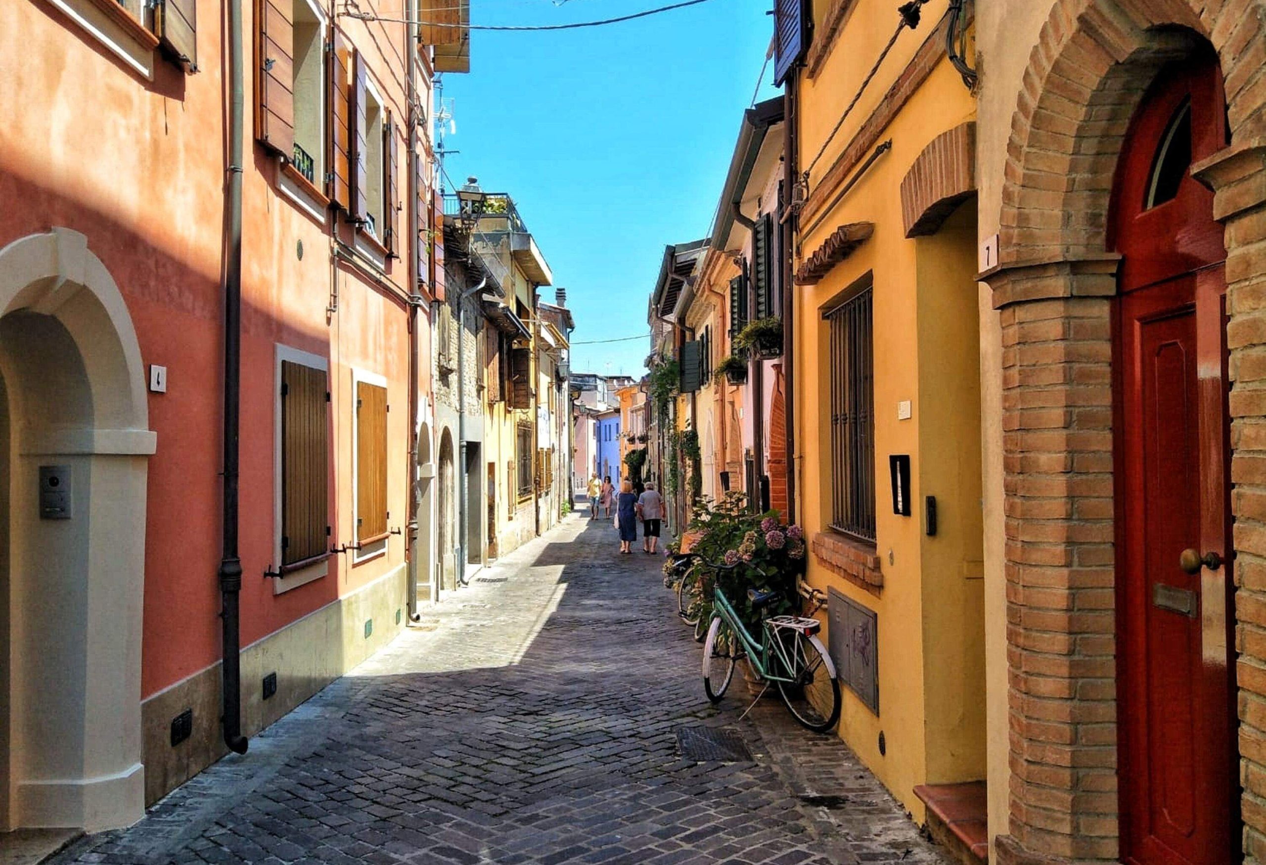 People walking through an alleyway lined with beautiful ancient buildings with arched doors.