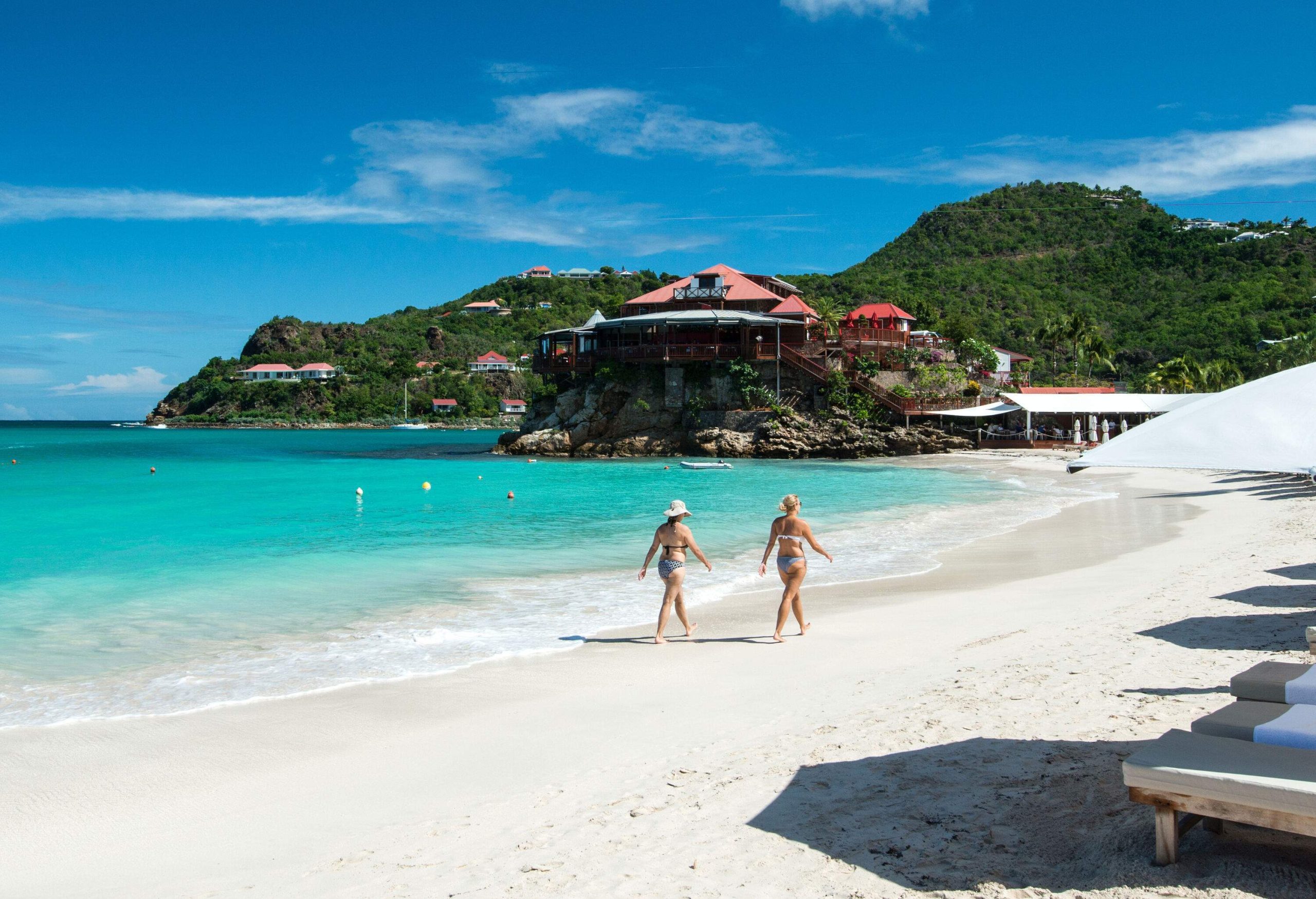 Two women in bikinis strolling down a white sand beach.