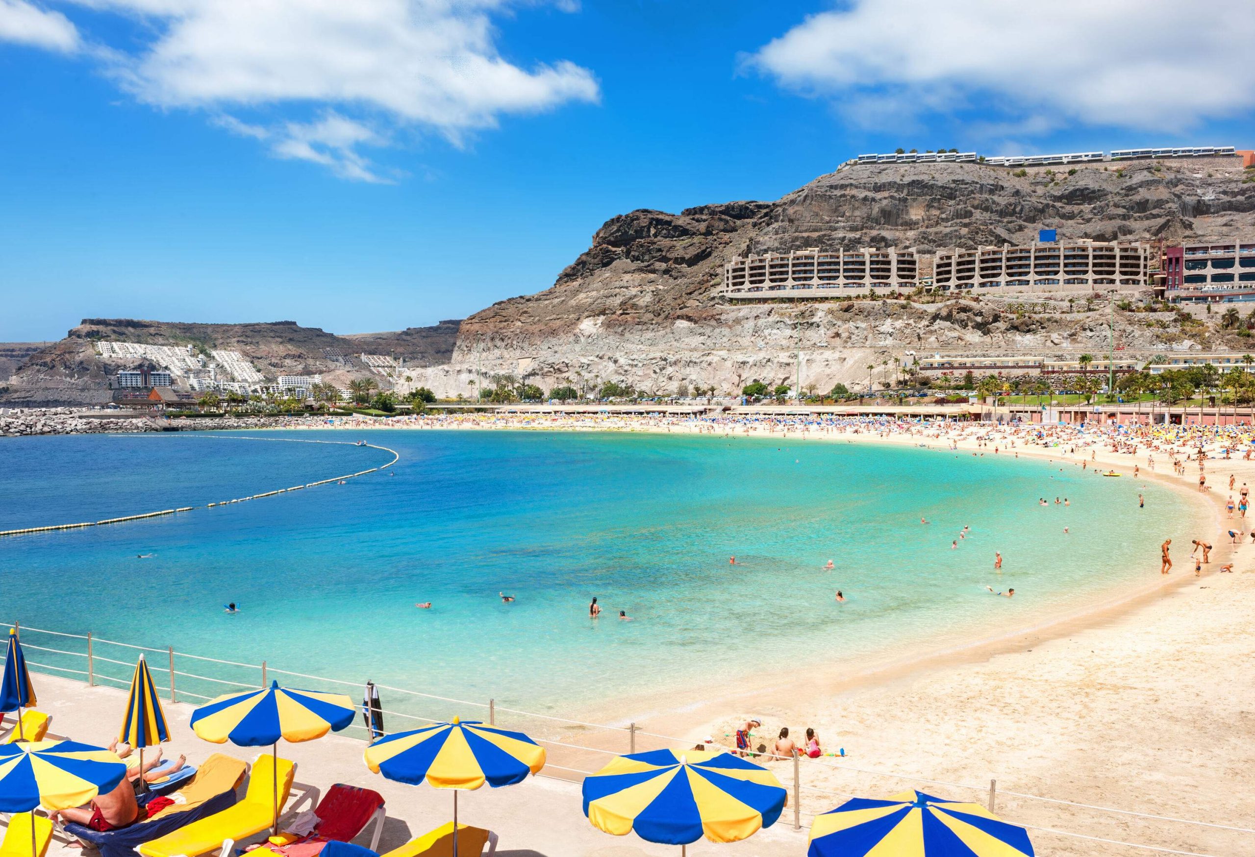 A crowd of people and colourful parasols on the shore of the tranquil clear water beach.