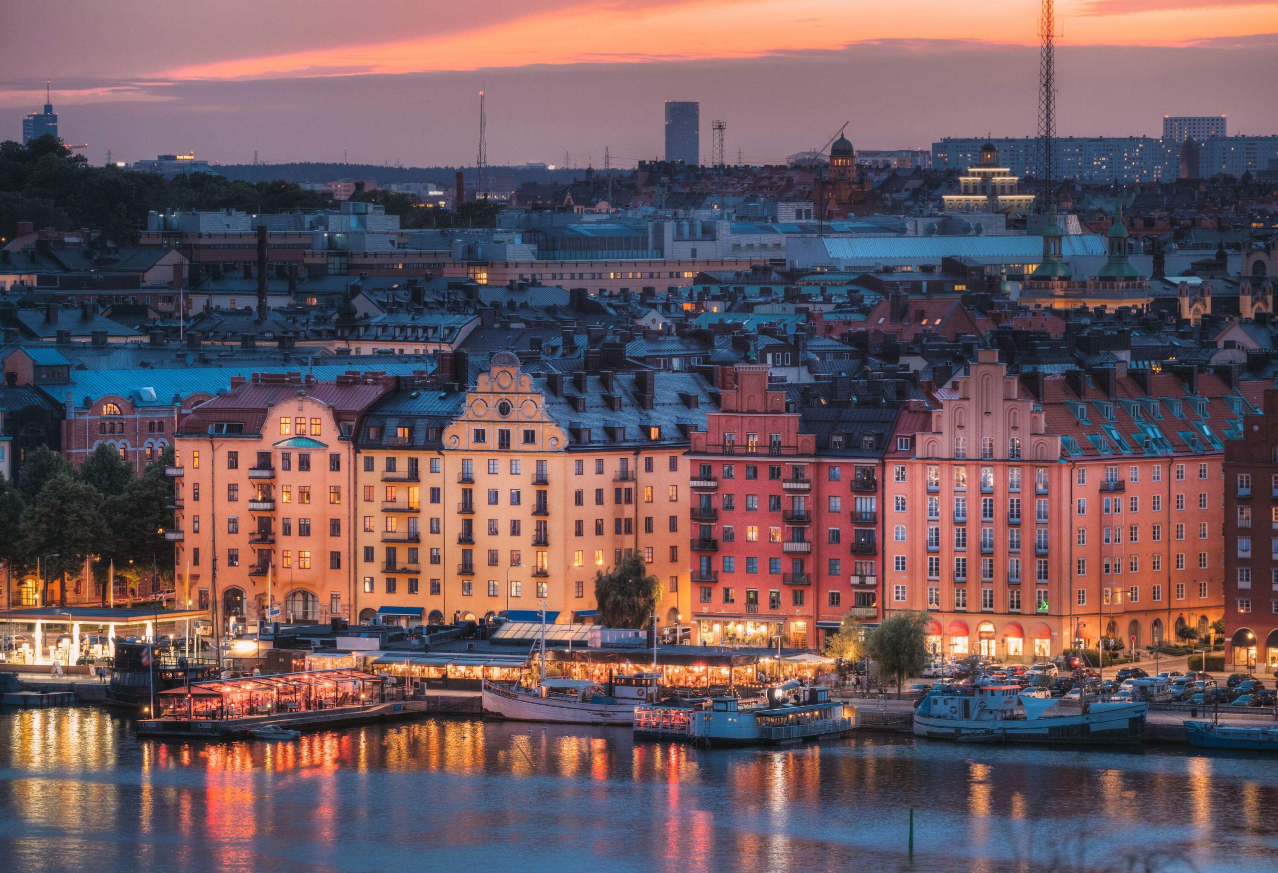 Night-time view of a harbour with anchored ferries along the illuminated waterfront buildings and the city's urban landscape.