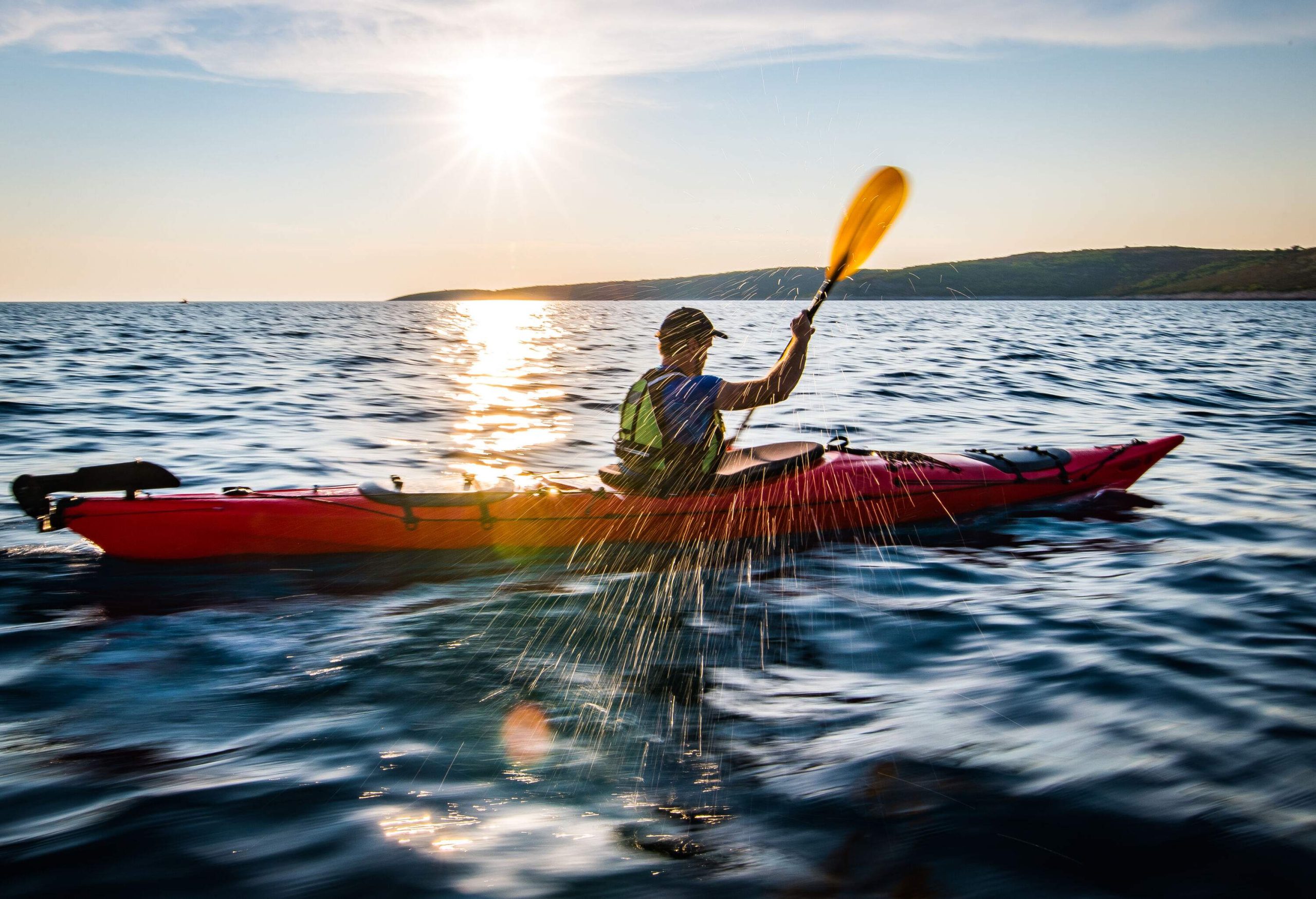 A kayaker paddles across a big ocean as the sun glistens on the waters.