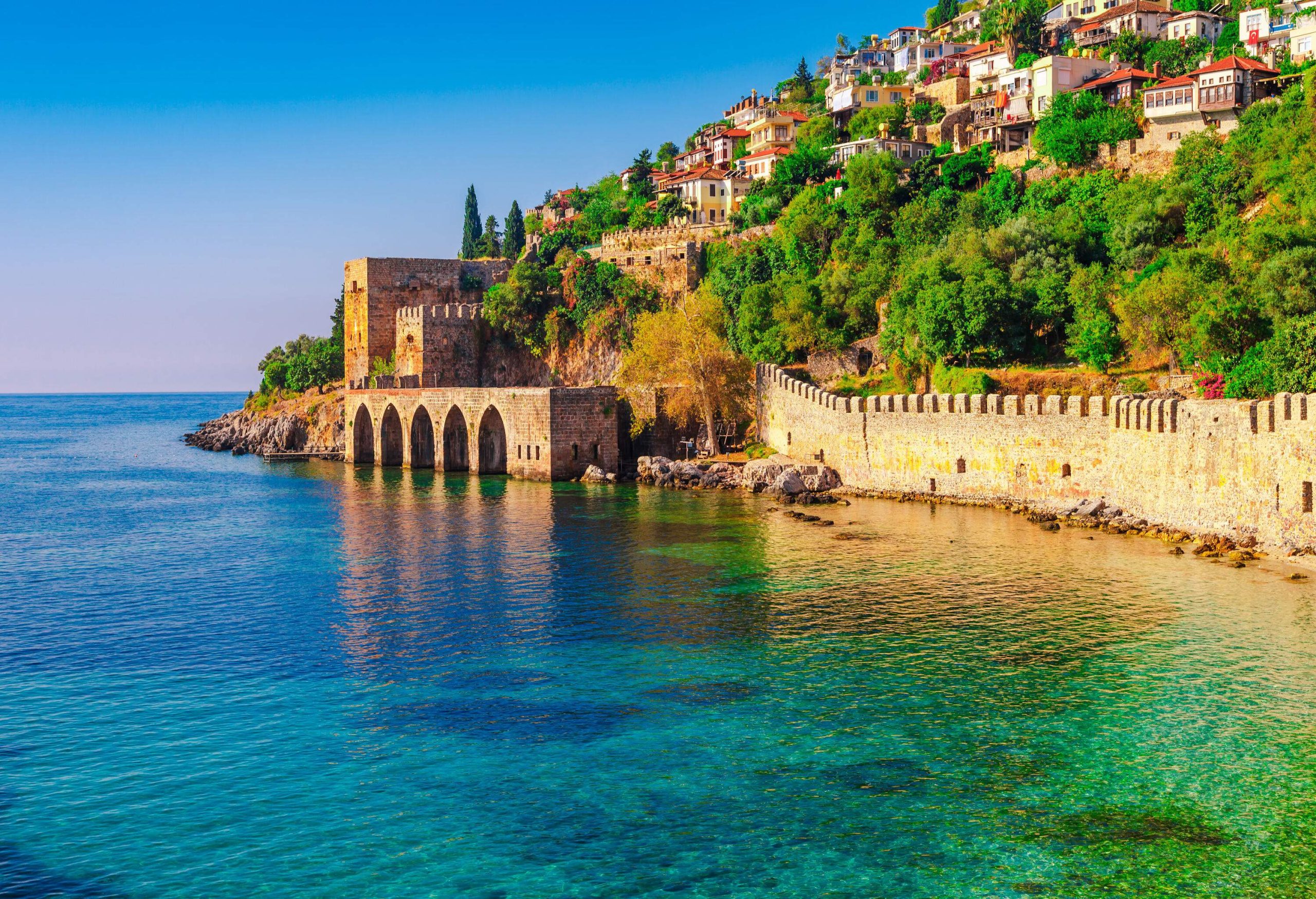 An ancient shipyard with arched foundation along a steep coastline with a cluster of buildings perched on the hillsides.