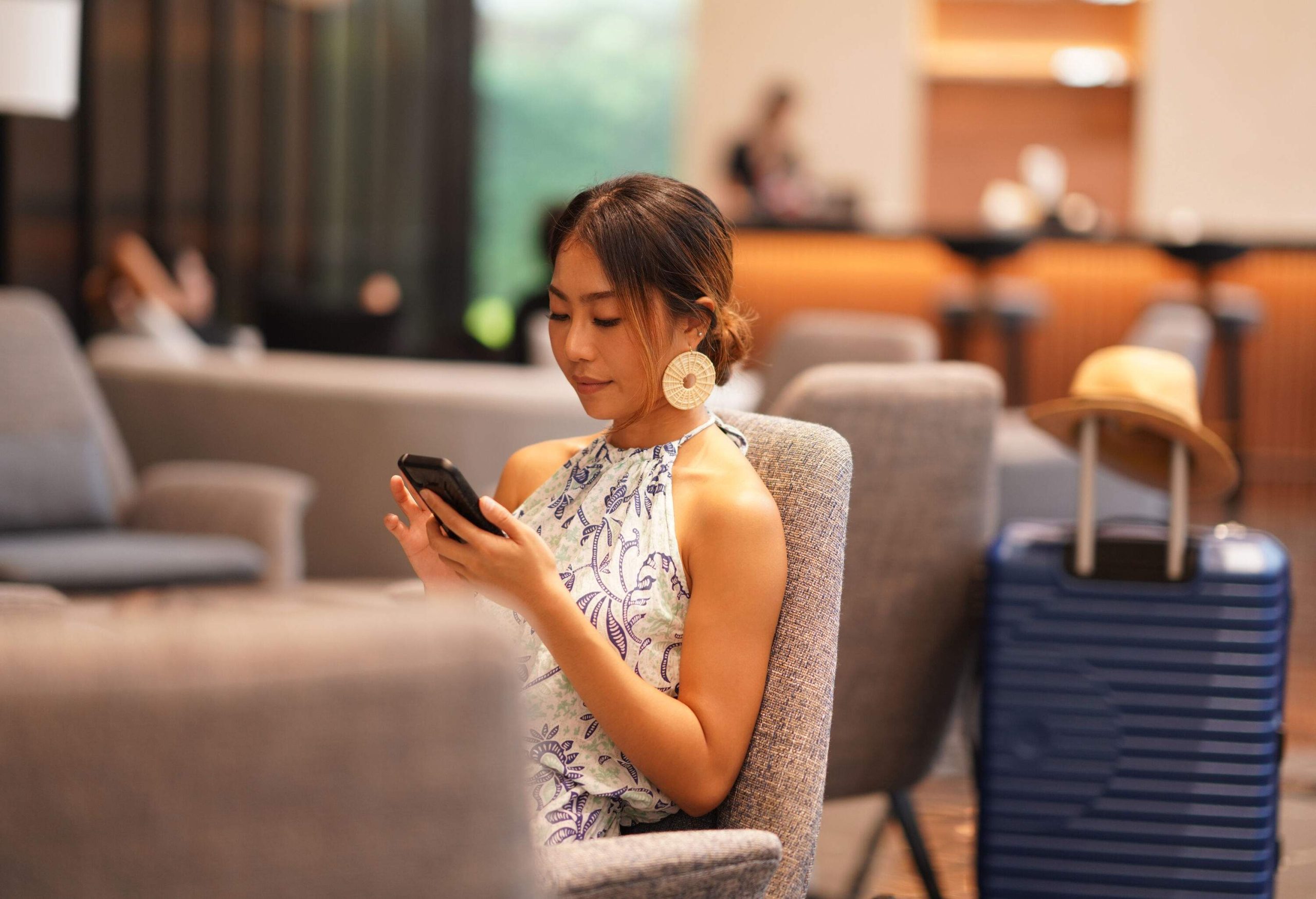 Asian young woman sitting at airport terminal lounge and using phone to chatting
