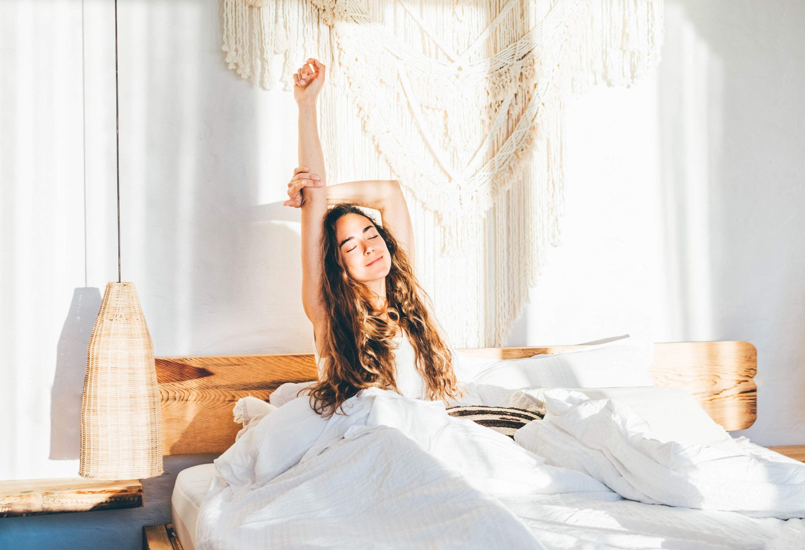 A woman stretching her hands while sitting on a bed.