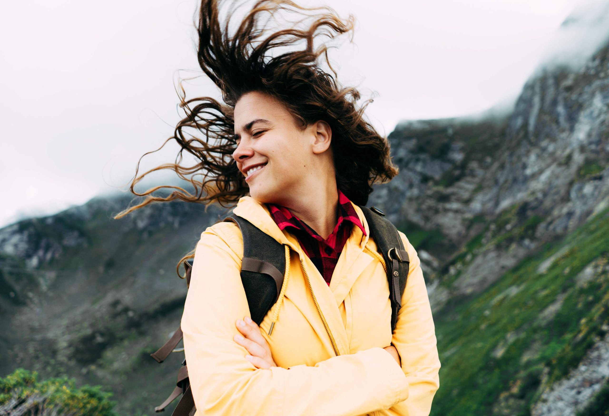 a young woman smiling with closed eyed while being in nature with wind in her hair