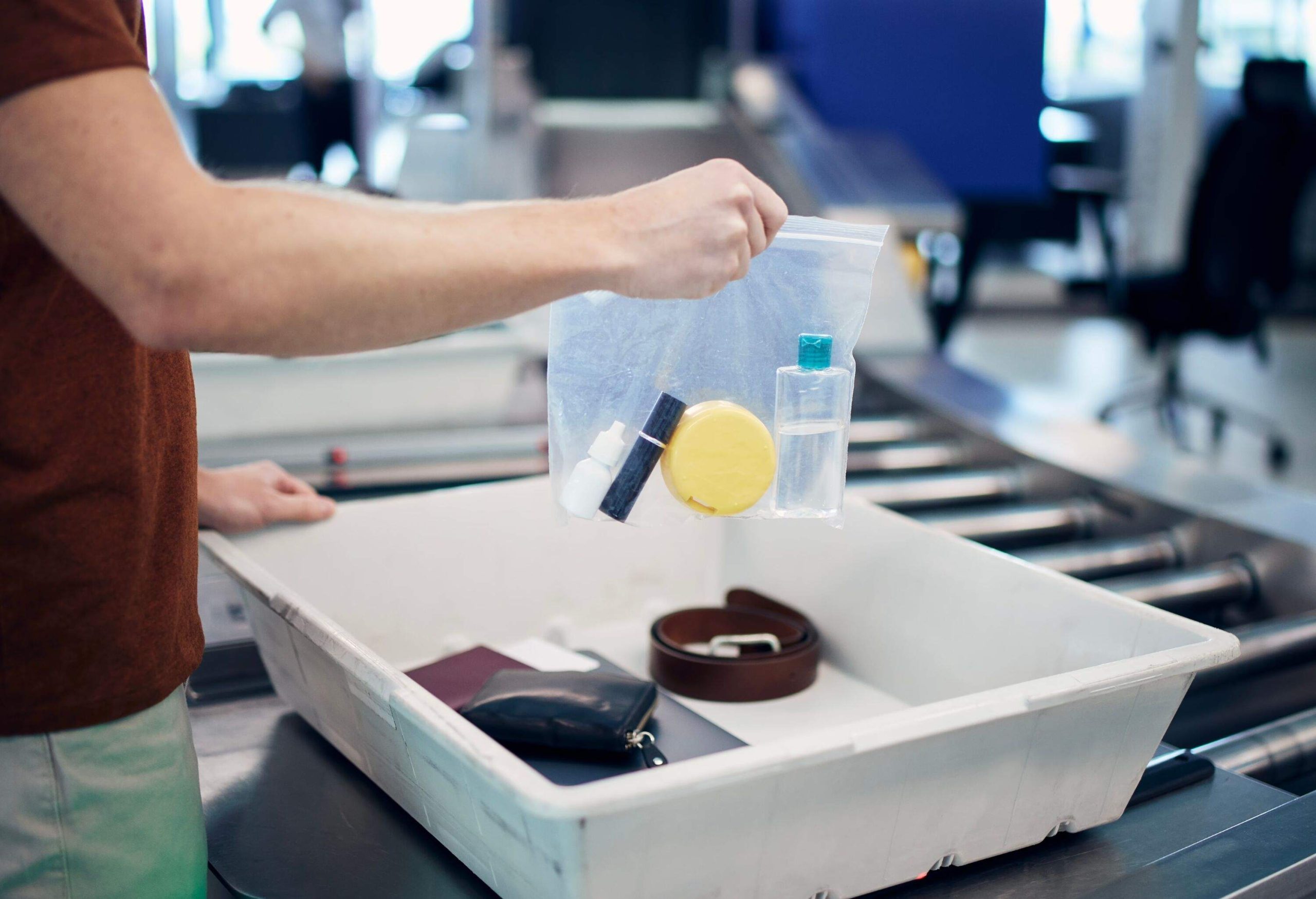 Airport security check before flight. Passenger holding plastic bag with liquids above container with laptop and personal items.