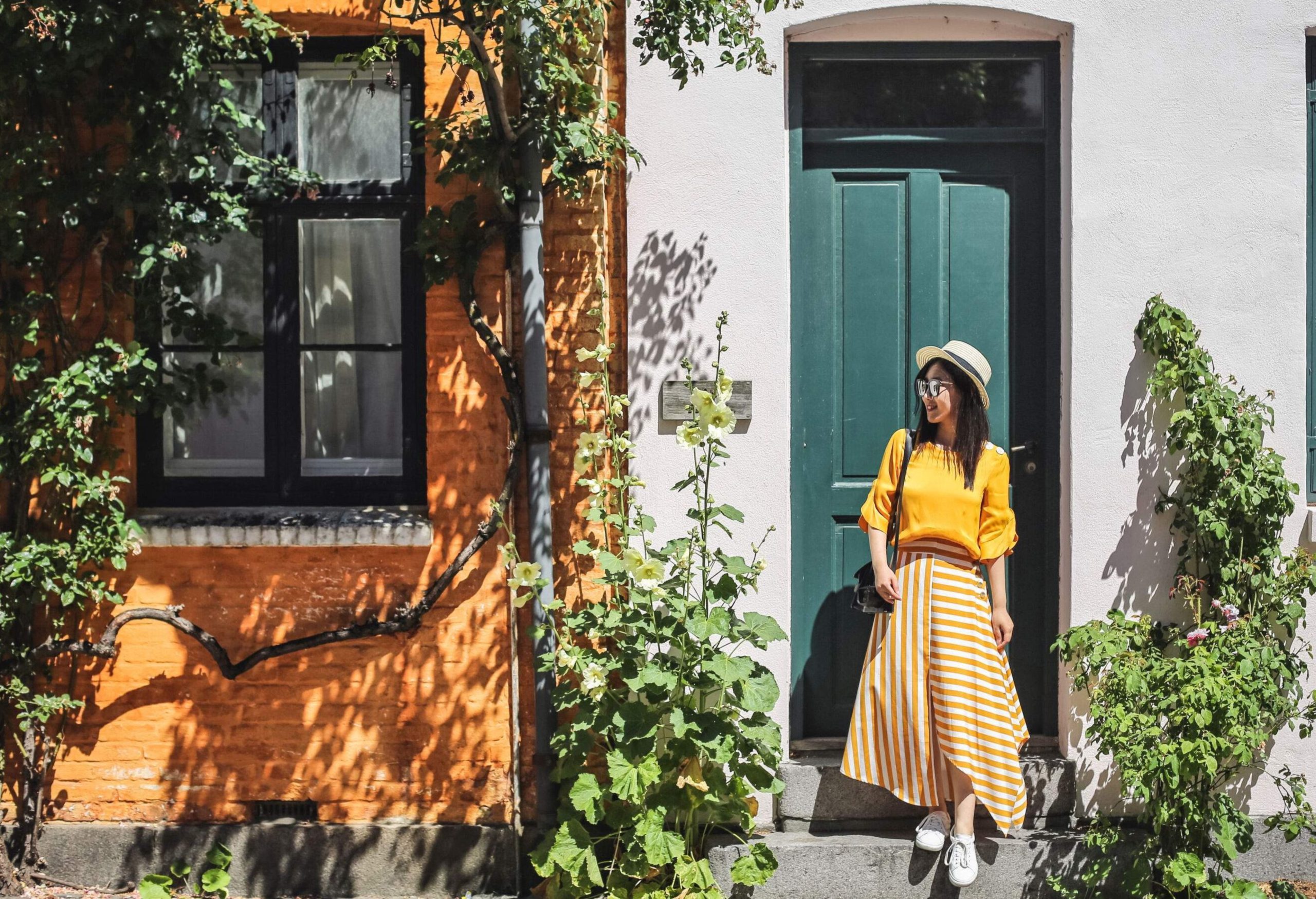 A smiling young lady steps down in front of a green door on a sunny day.