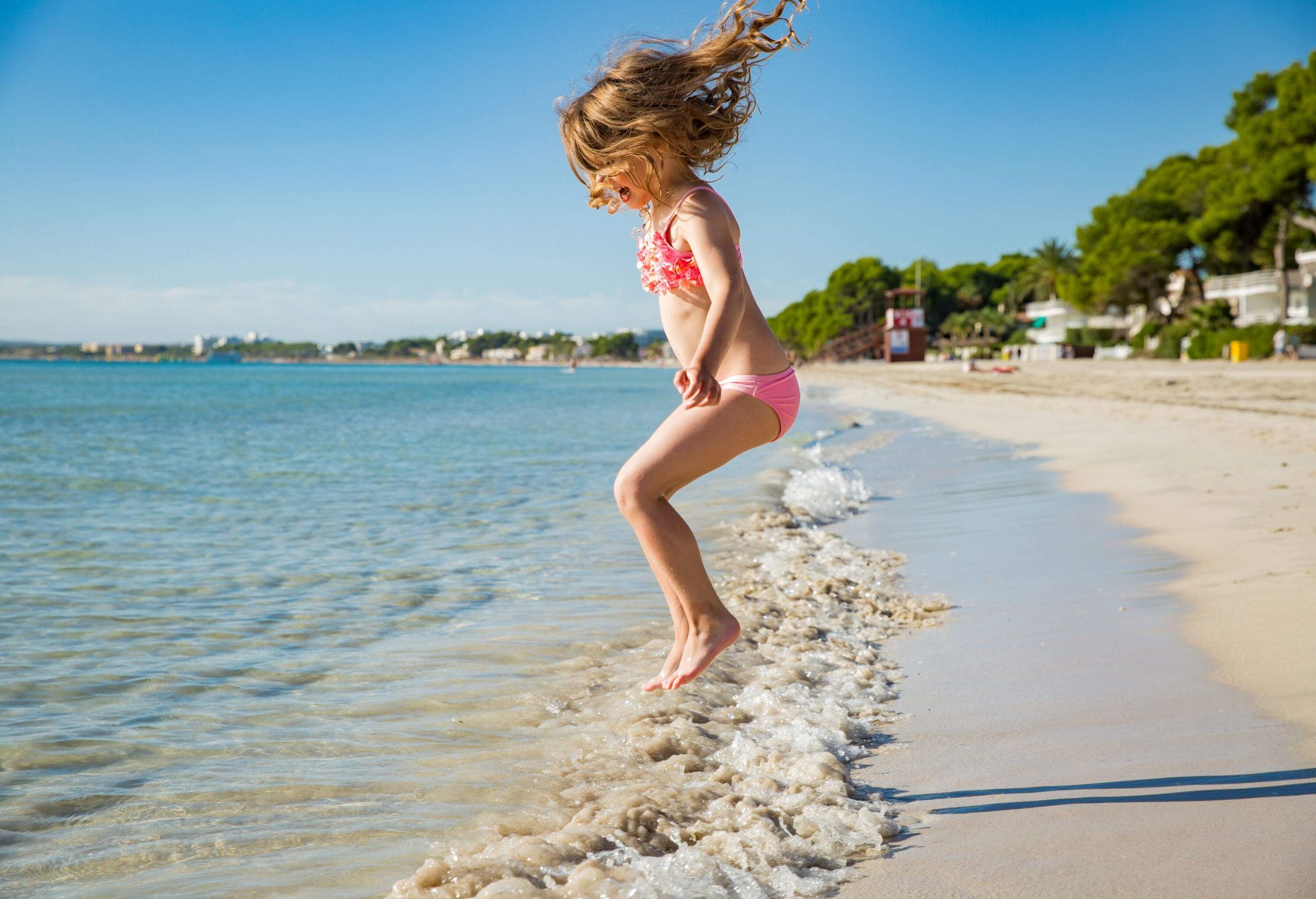 A brunette girl in a bathing suit jumps over the beach waves.