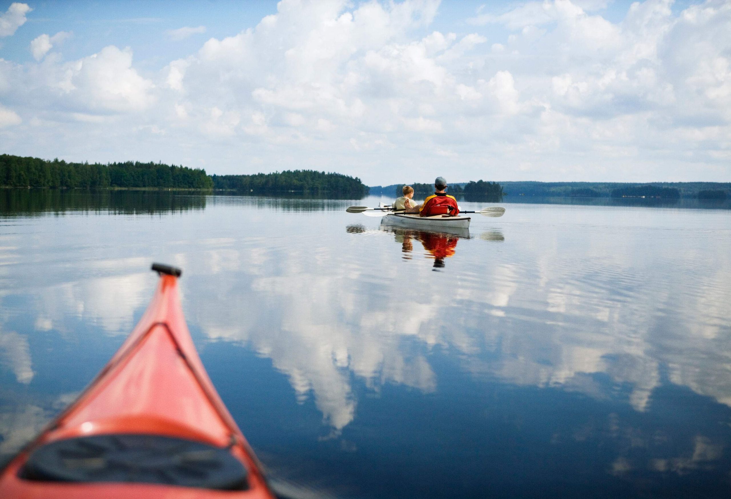 Two people canoeing on a crystal-clear lake under billowing clouds.