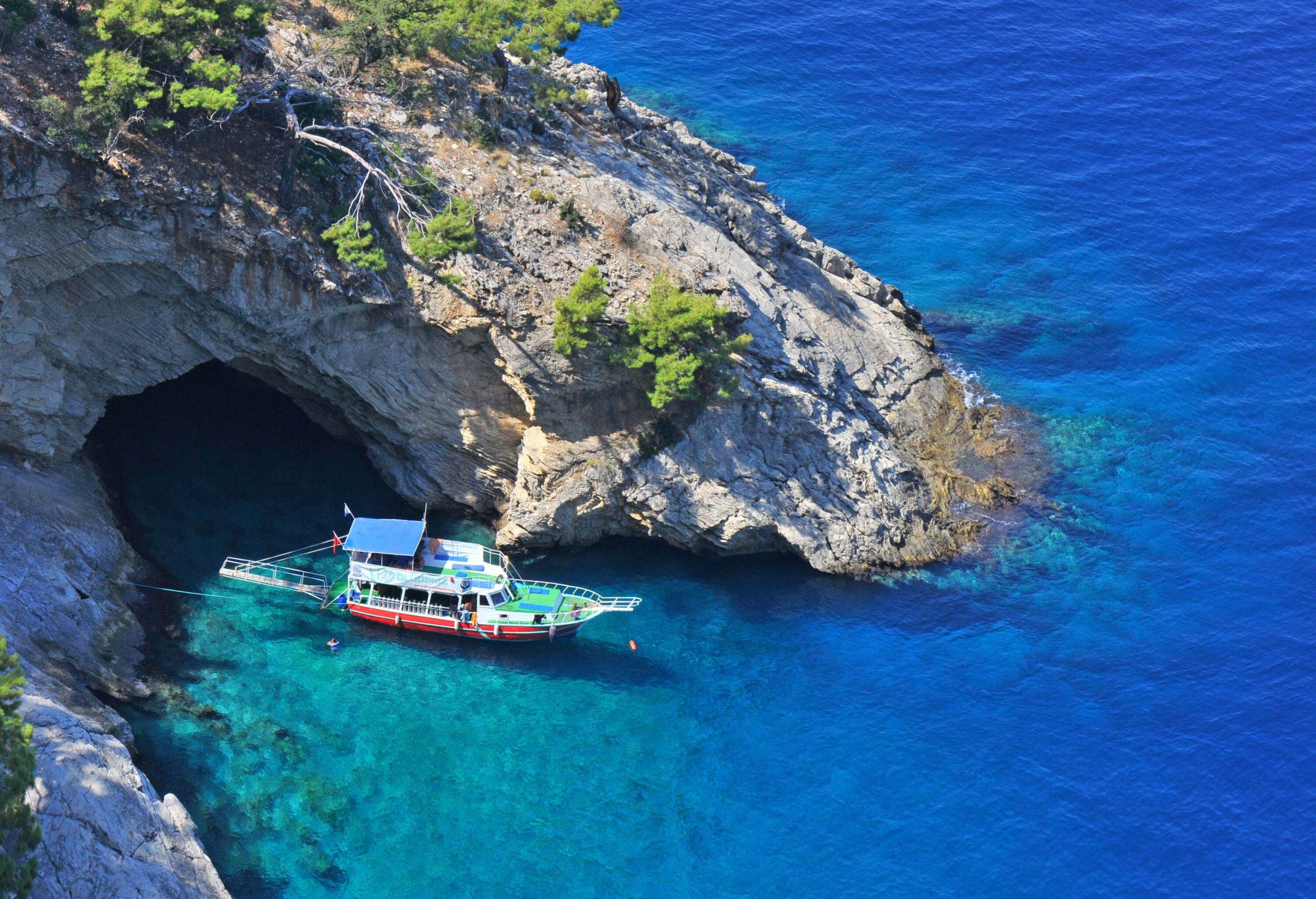 A gulet moored by the rugged, cave-like coast.