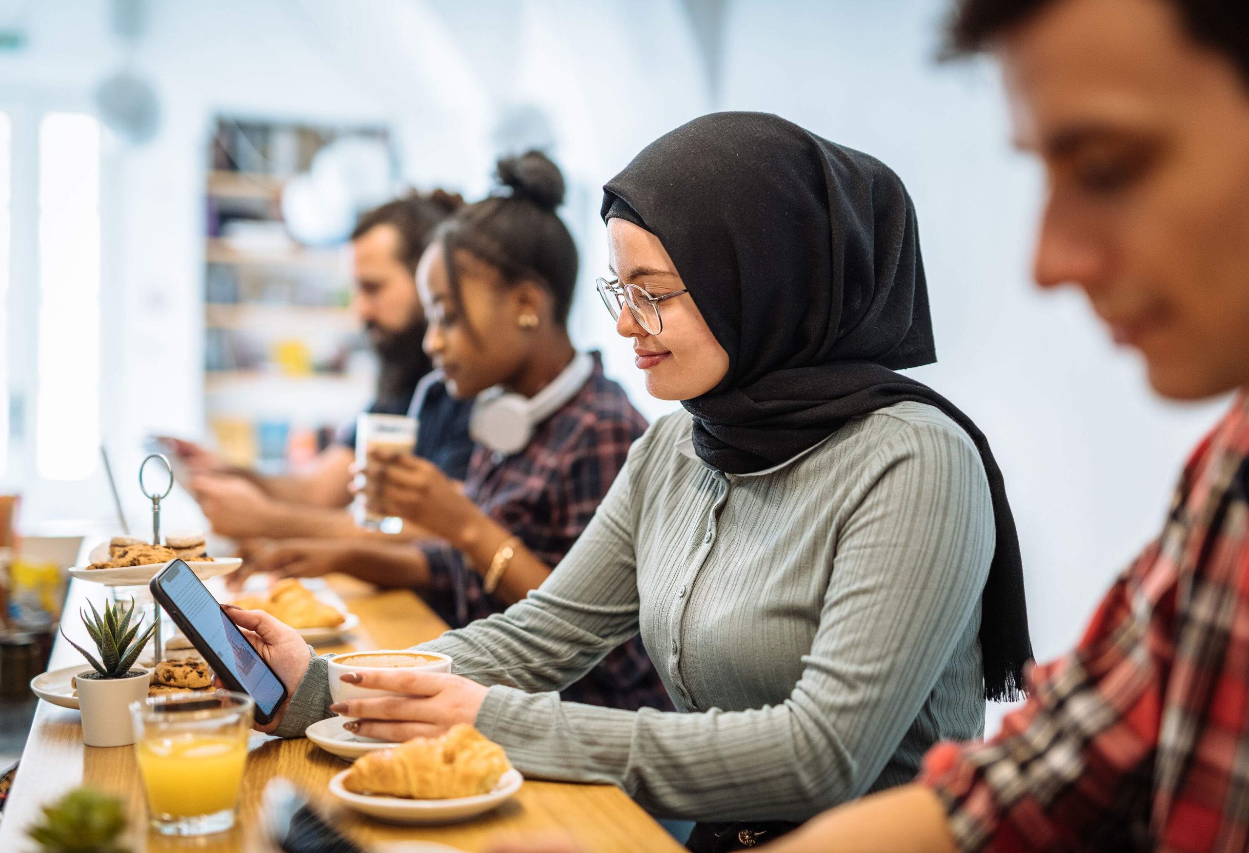 A woman in a black hijab sits on a café with her friends while having breakfast.