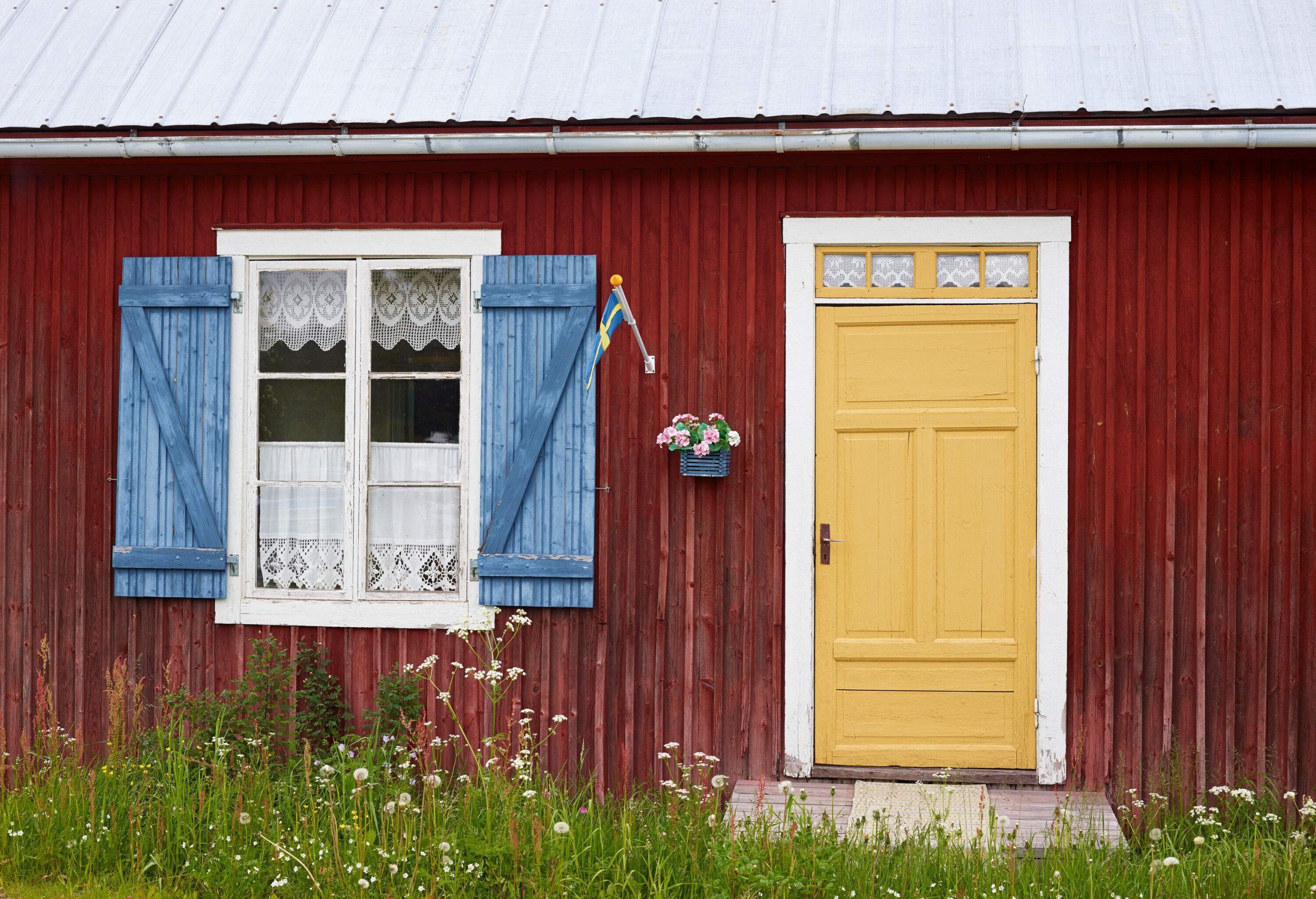 A colourful wooden cottage with unkempt grass in front of it.