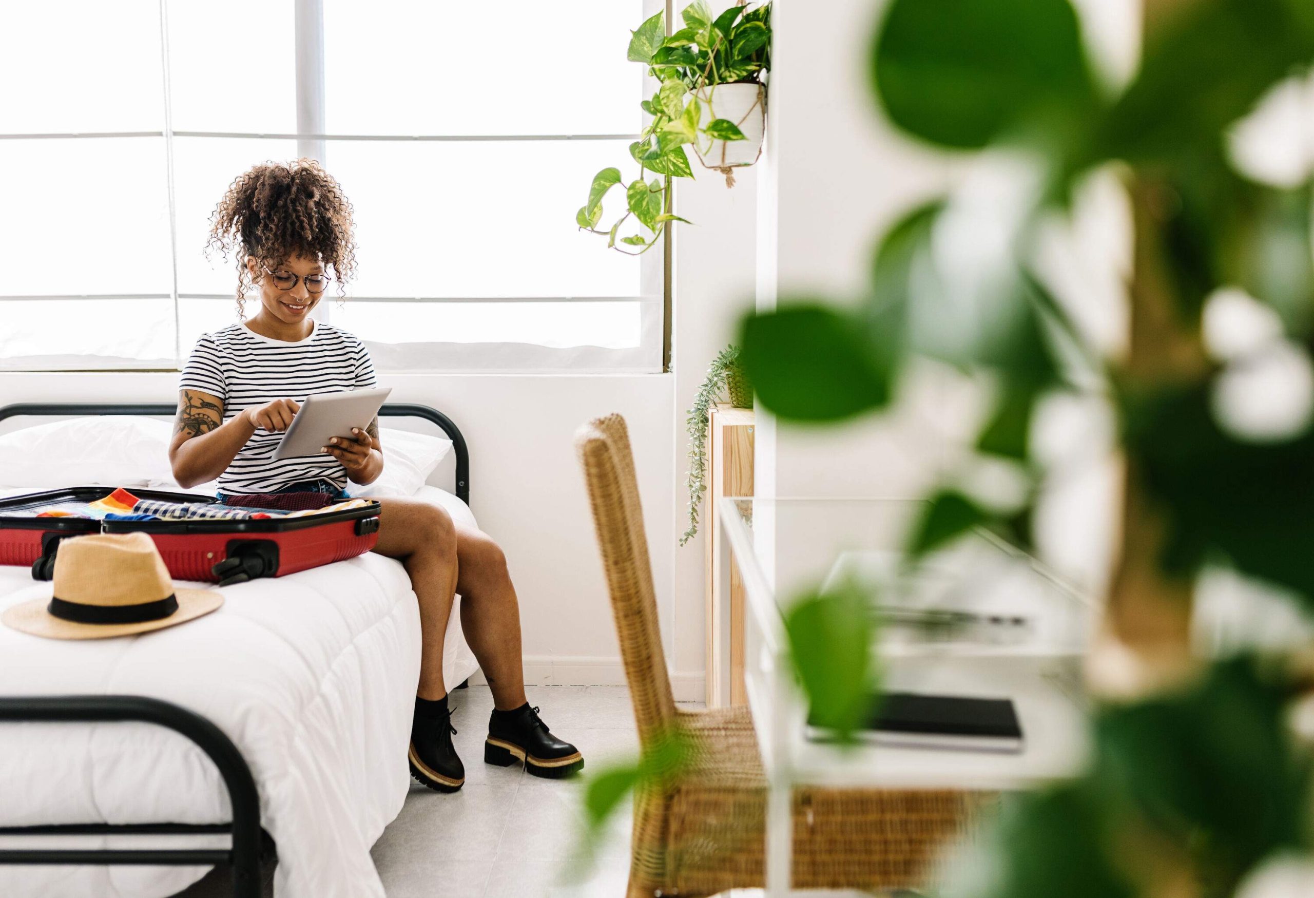 A woman sitting on the bed with her luggage, using her tablet computer.