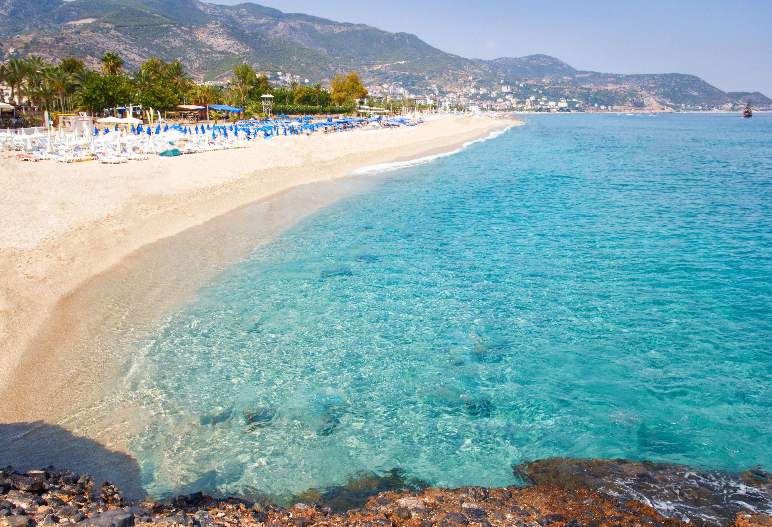 A serene tropical resort featuring a sea beach during the summer with sea beds lining the shore and a verdant mountain range in the distance.