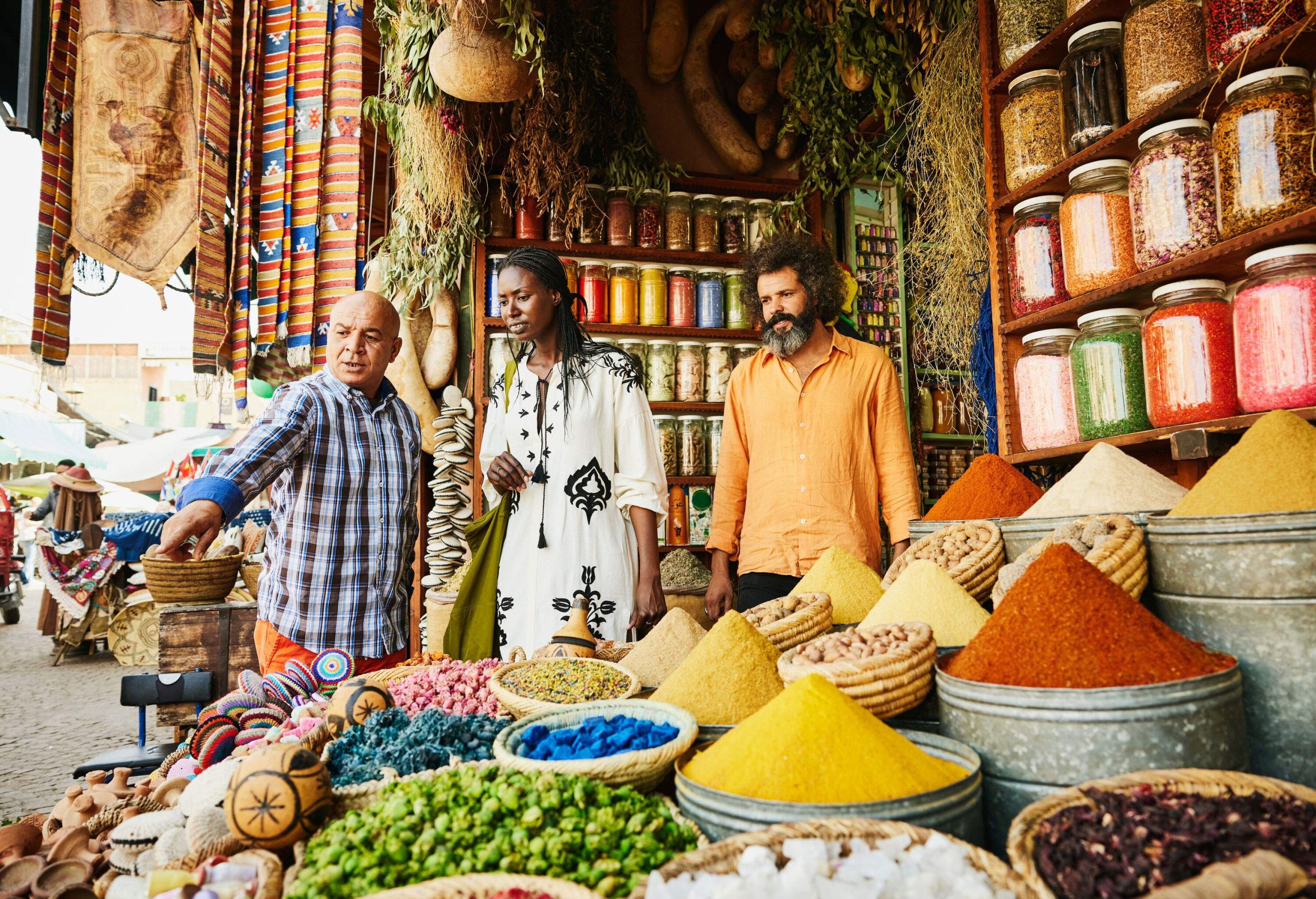 Wide shot of couple talking to shop owner while shopping in spice shop in the souks of Marrakech during vacation