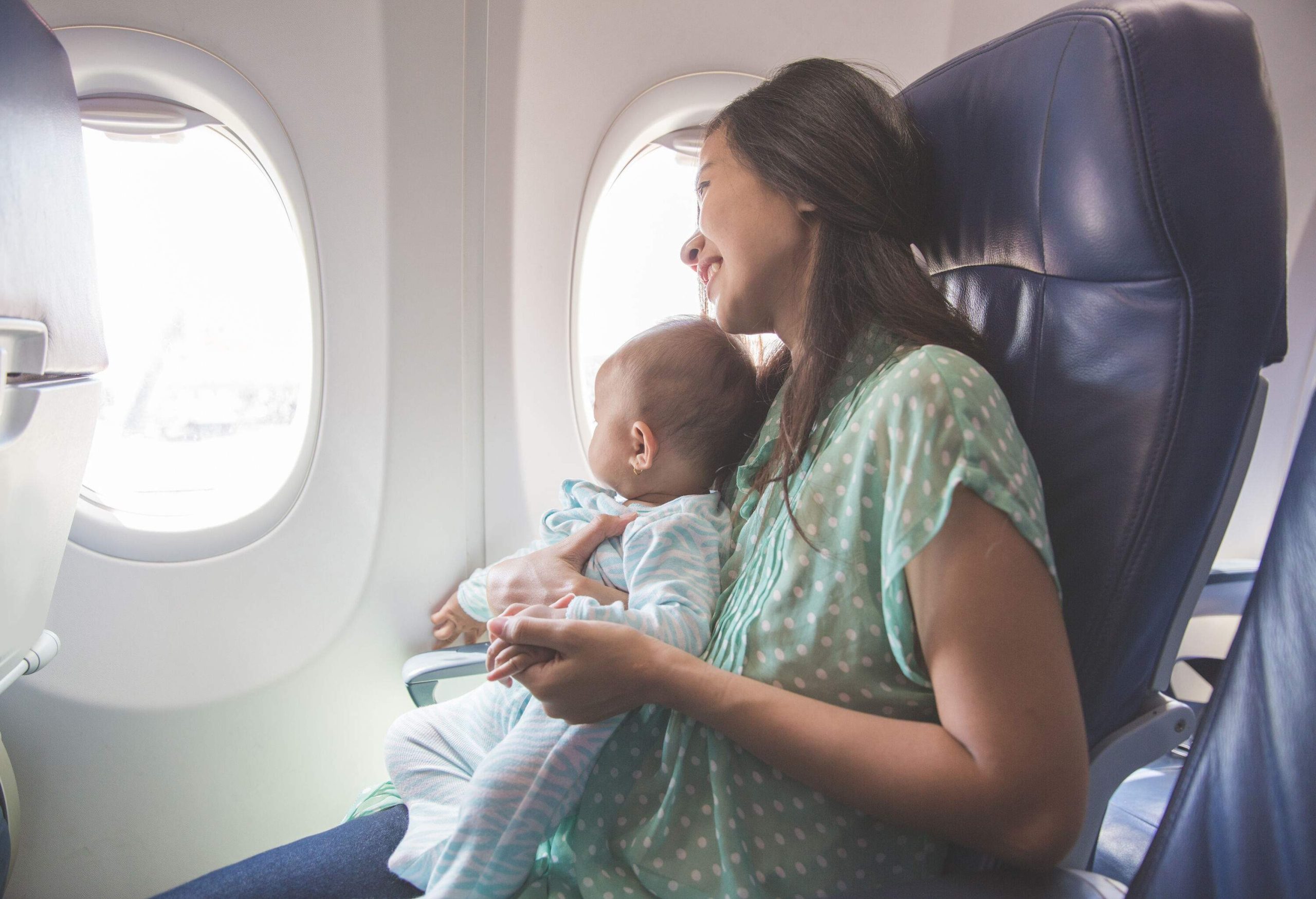 A mother and a baby on the plane seated next to the window.