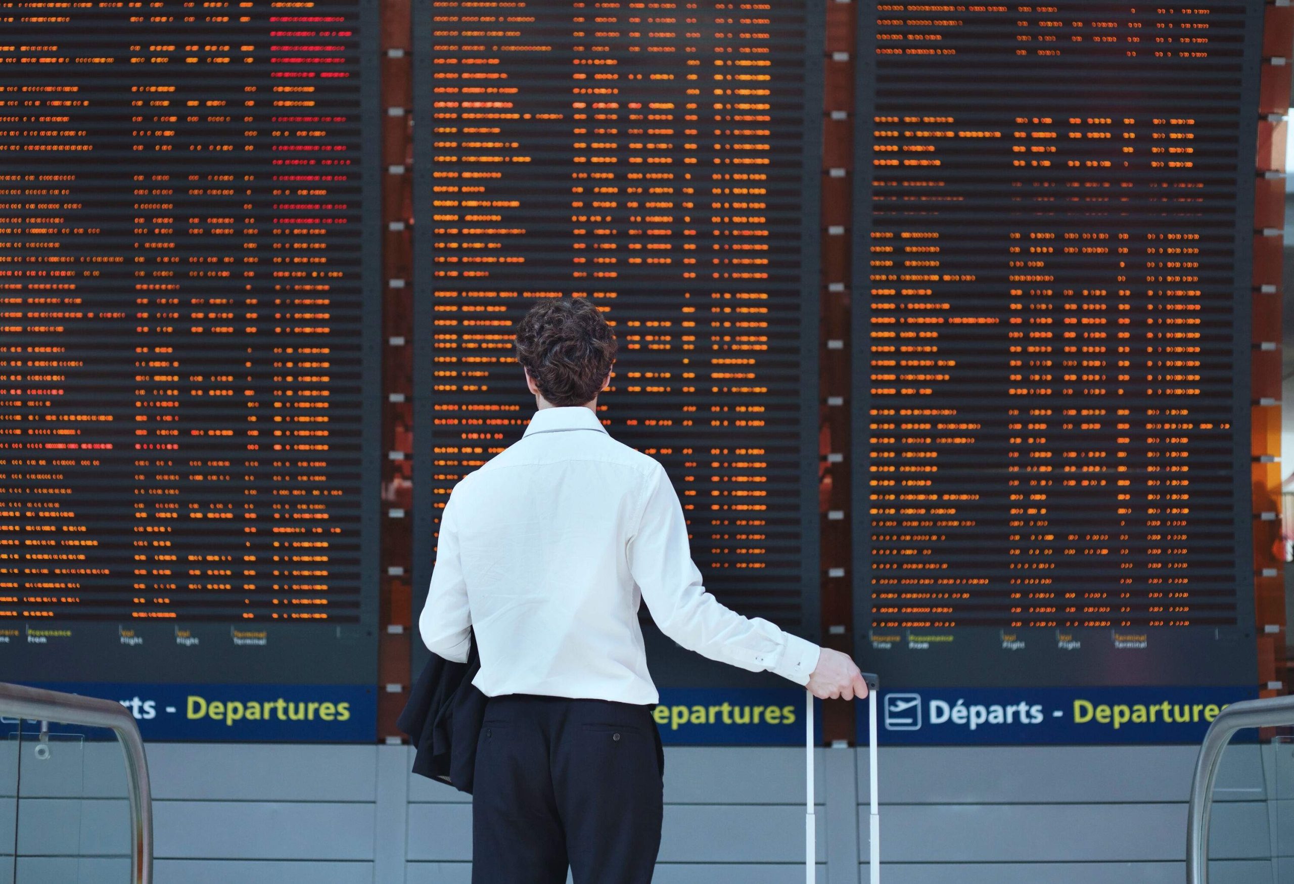 A passenger with luggage checking the flight information display system at the airport for flight details.