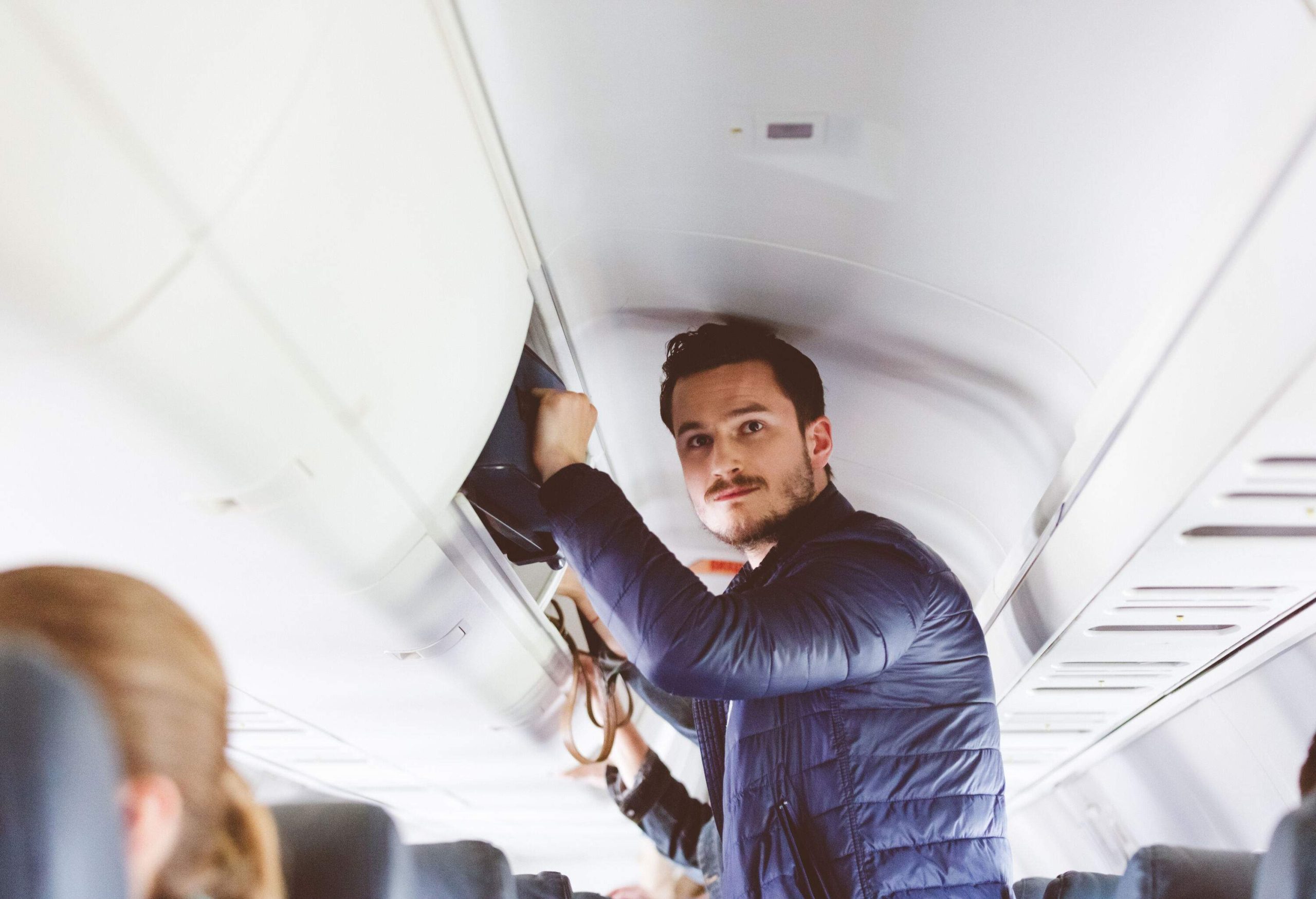 A tall and attractive man securing his luggage into the overhead bin.