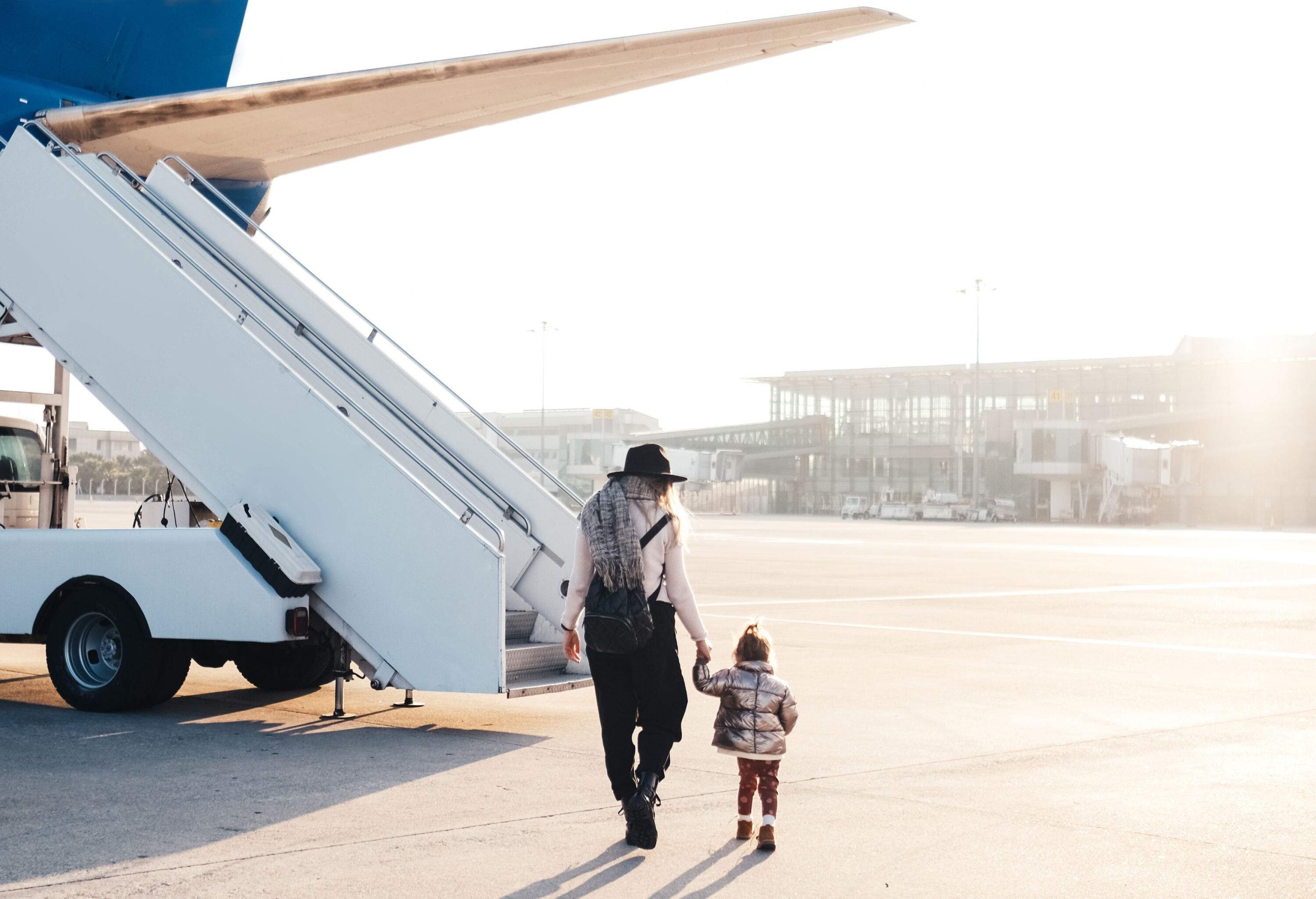 A person and kid in casual clothes hold hands while walking towards the plane's stairs.