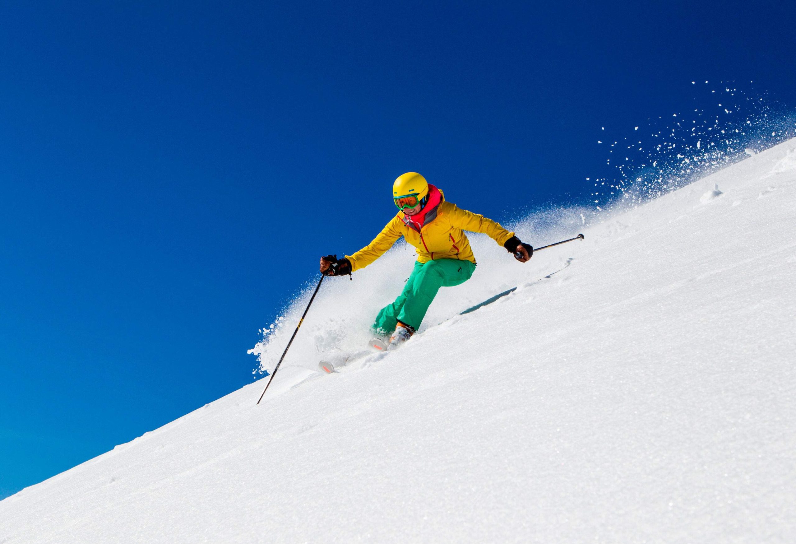 A female skier slides down a snow-covered hill with a background of a cloudless blue sky.