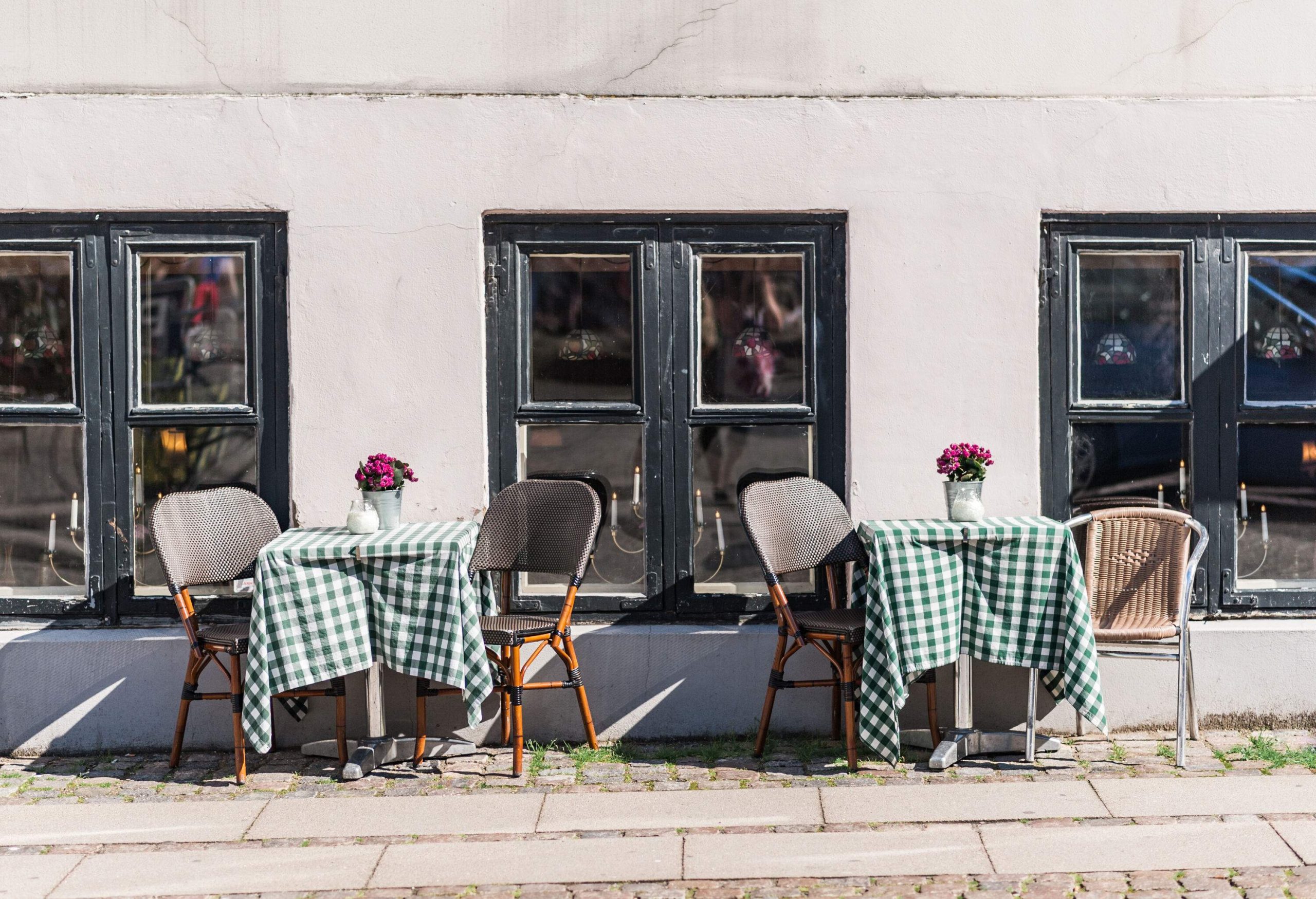 Two sets of tables and chairs with floral centrepieces on a sidewalk.