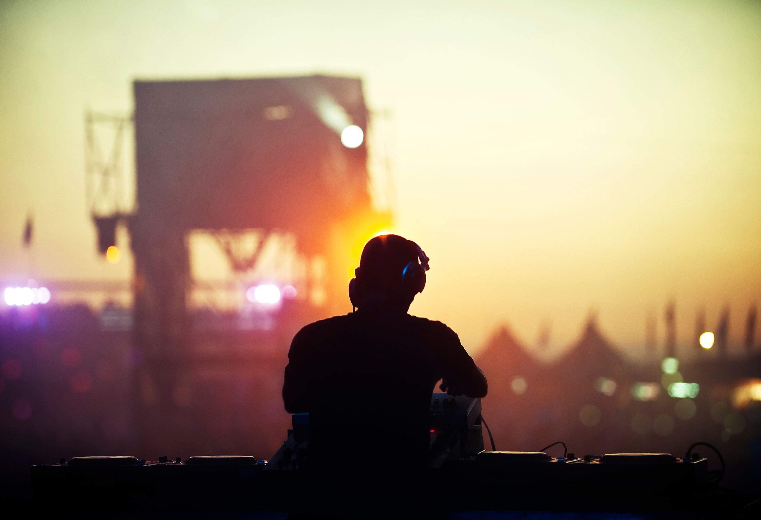 A DJ performing on stage with silhouette of buildings in the background.